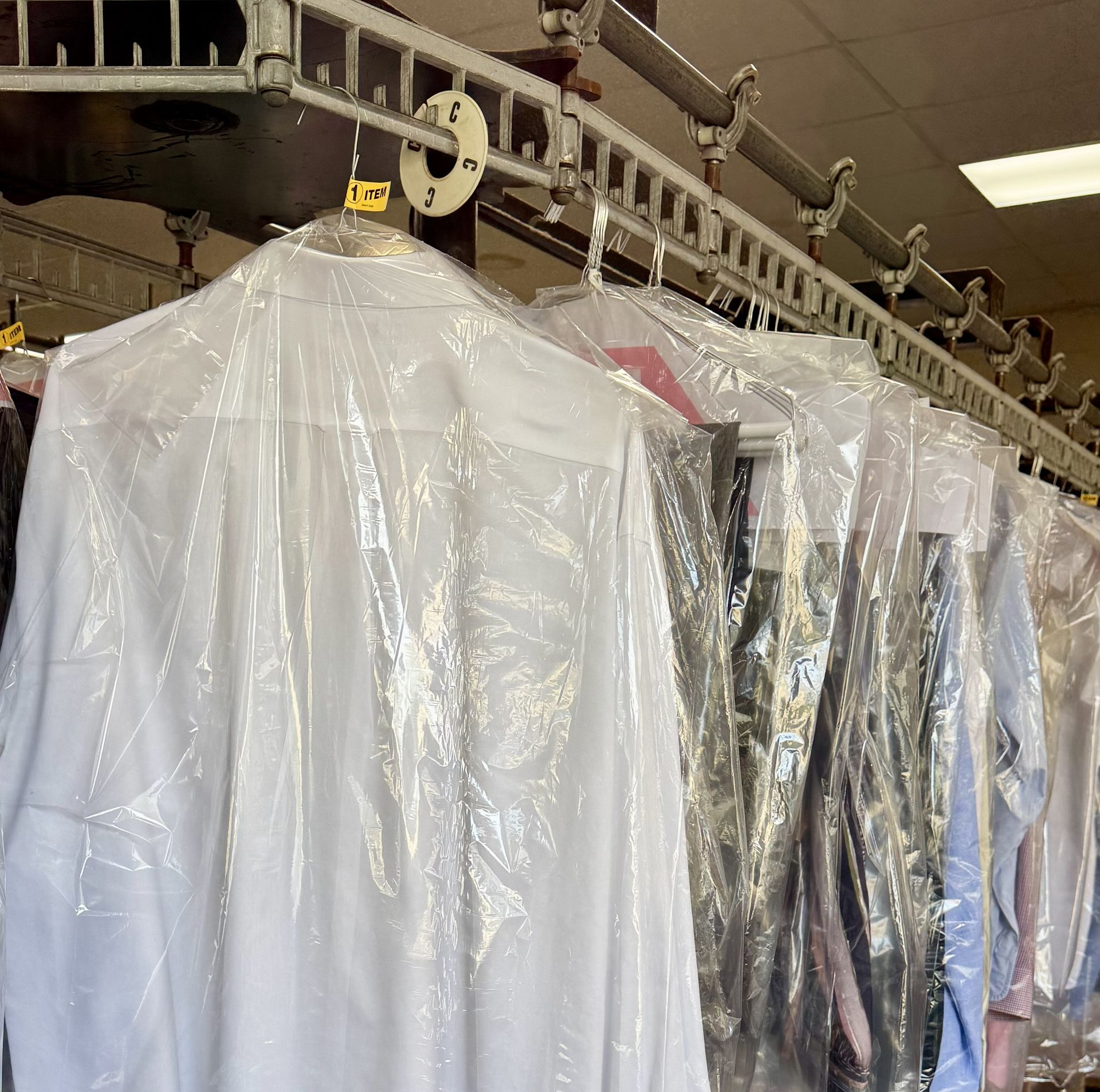 A row of freshly dry-cleaned dress shirts in plastic garment bags hanging on a motorized rack in a laundry service.