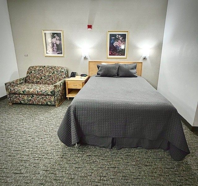 A hotel room with a bed, floral couch, bedside table, and artwork; neutral colors.