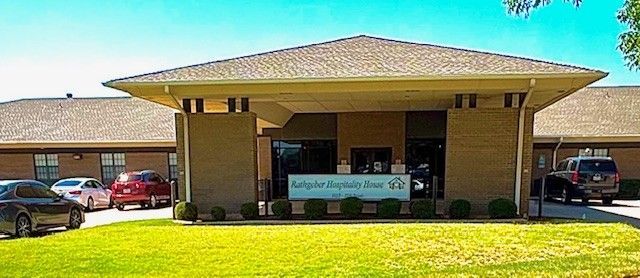 Exterior view of the Samaritan Hospitality House with parked cars in front. Green lawn and blue sky.