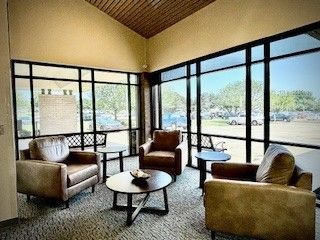 Lounge area with three brown leather armchairs, small tables, and large windows overlooking a parking lot.