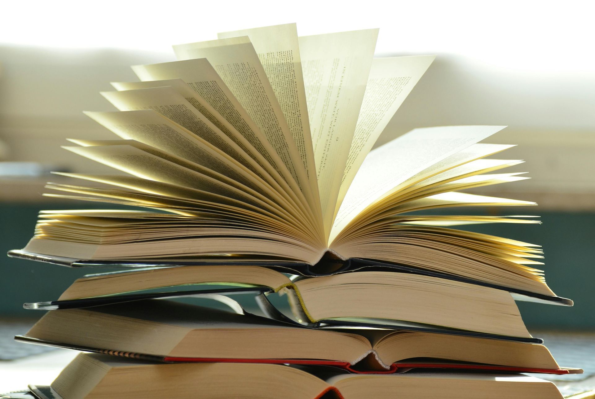 Books stacked with one open, pages fanned out. Sunlight illuminates the pages.