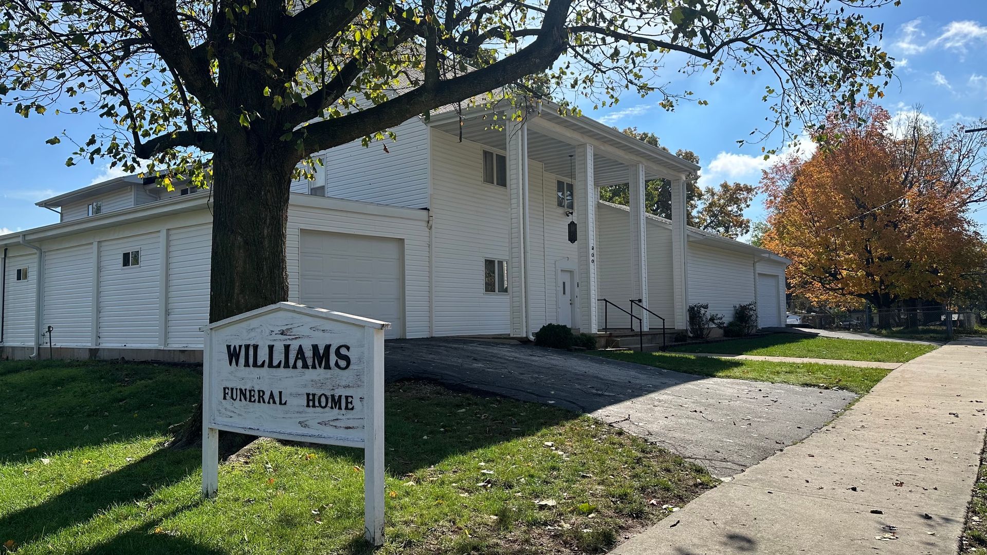 A wide, flat field of green grass with fall trees and a hazy sky in the background.