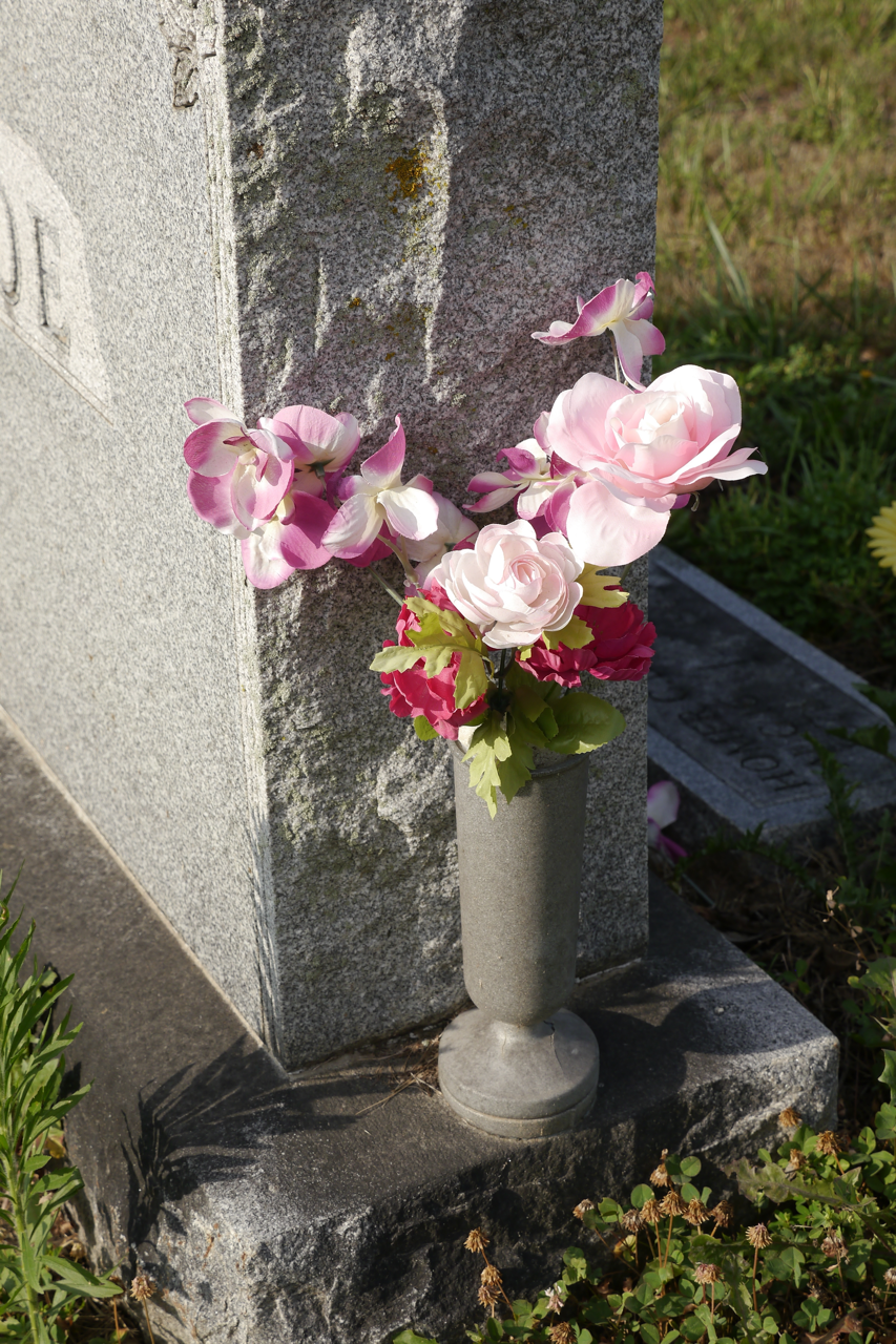 A memorial vase with pink flowers attached to a headstone