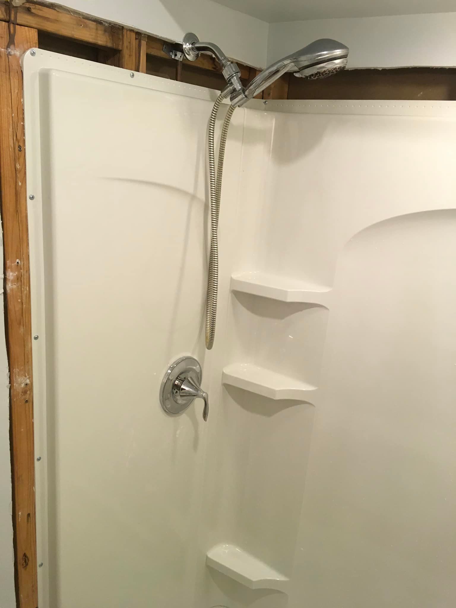 Aqua Plumbing Pros | A shower stall with a shower head and shelves in a bathroom.