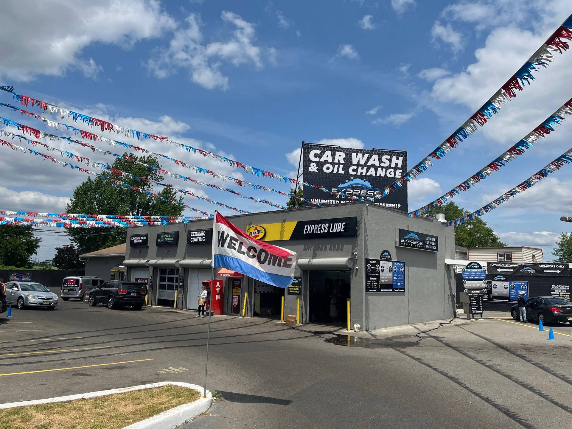 Car wash and oil change shop with cars waiting; blue sky and festive flags.