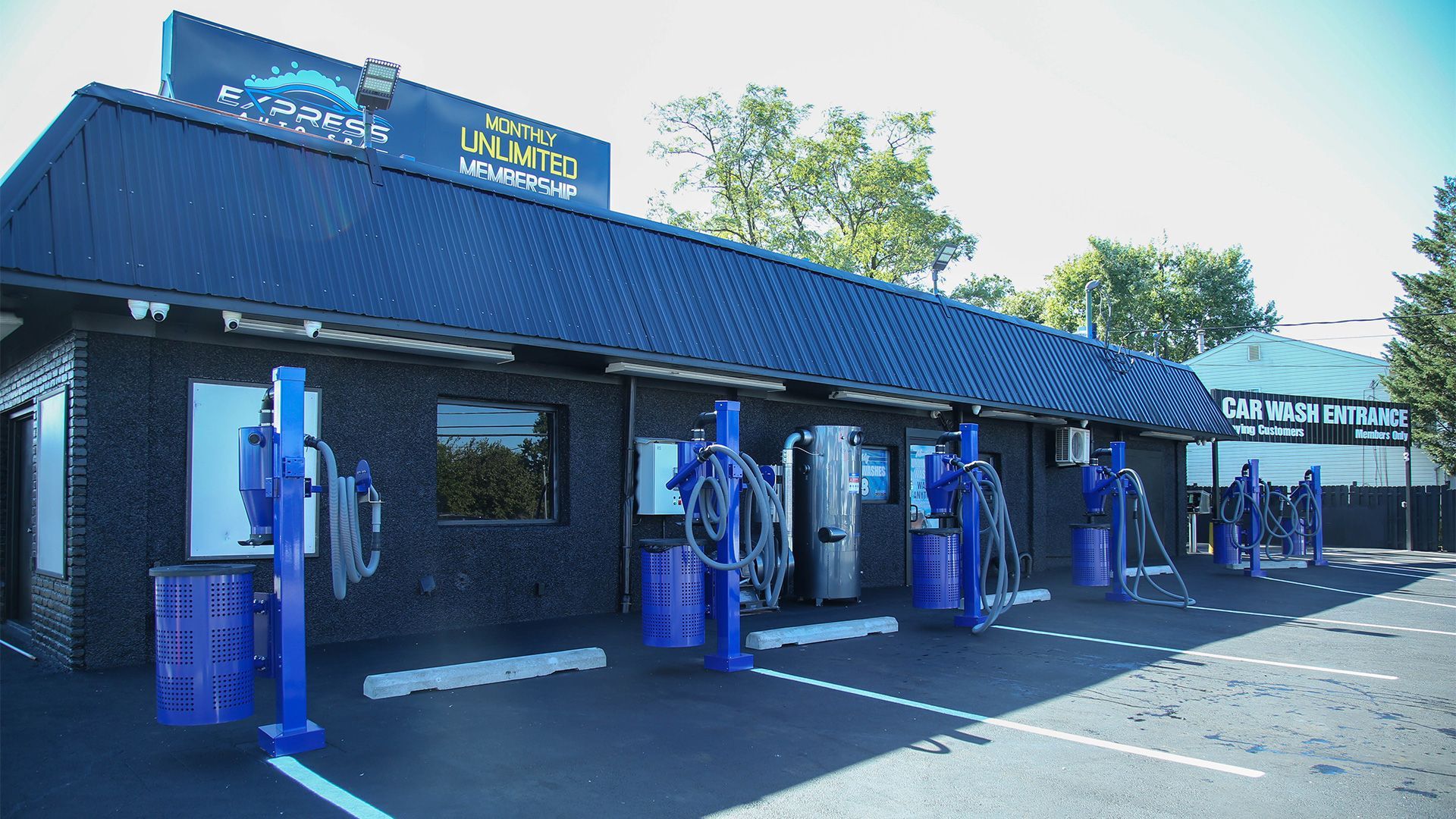 Car wash exterior with blue vacuum stations, dark building, and parking spaces.