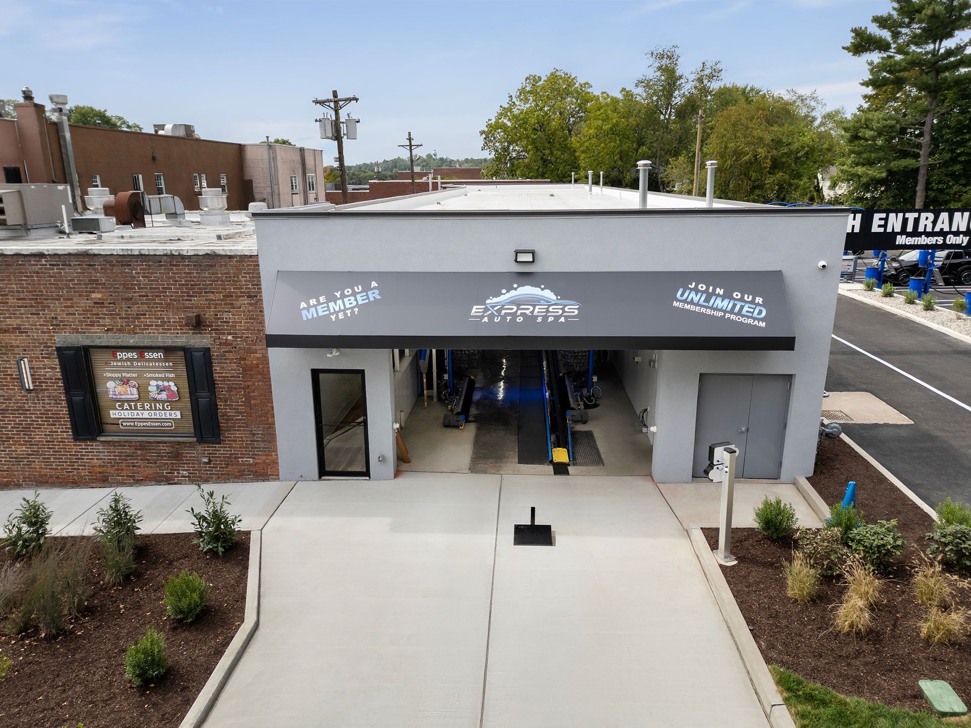 Exterior view of a car wash with a gray awning and entrance. A paved driveway leads into the wash bay.
