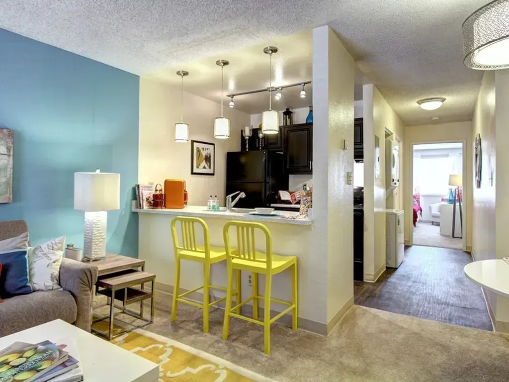 Open-plan living room with blue walls, yellow stools at a breakfast bar, and a bright hallway beyond