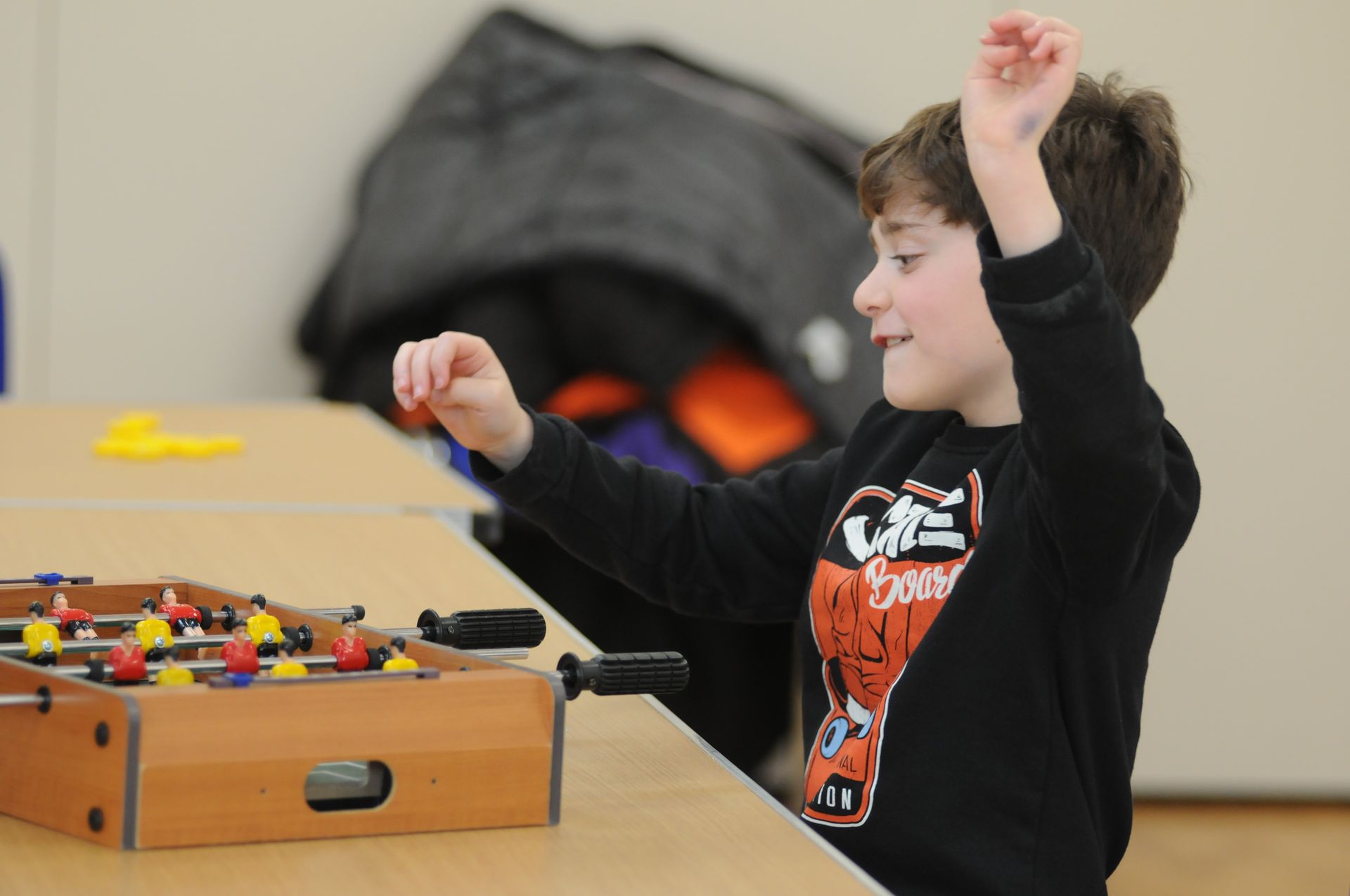 A young boy wearing a black shirt with a basketball on it is playing a game of foosball
