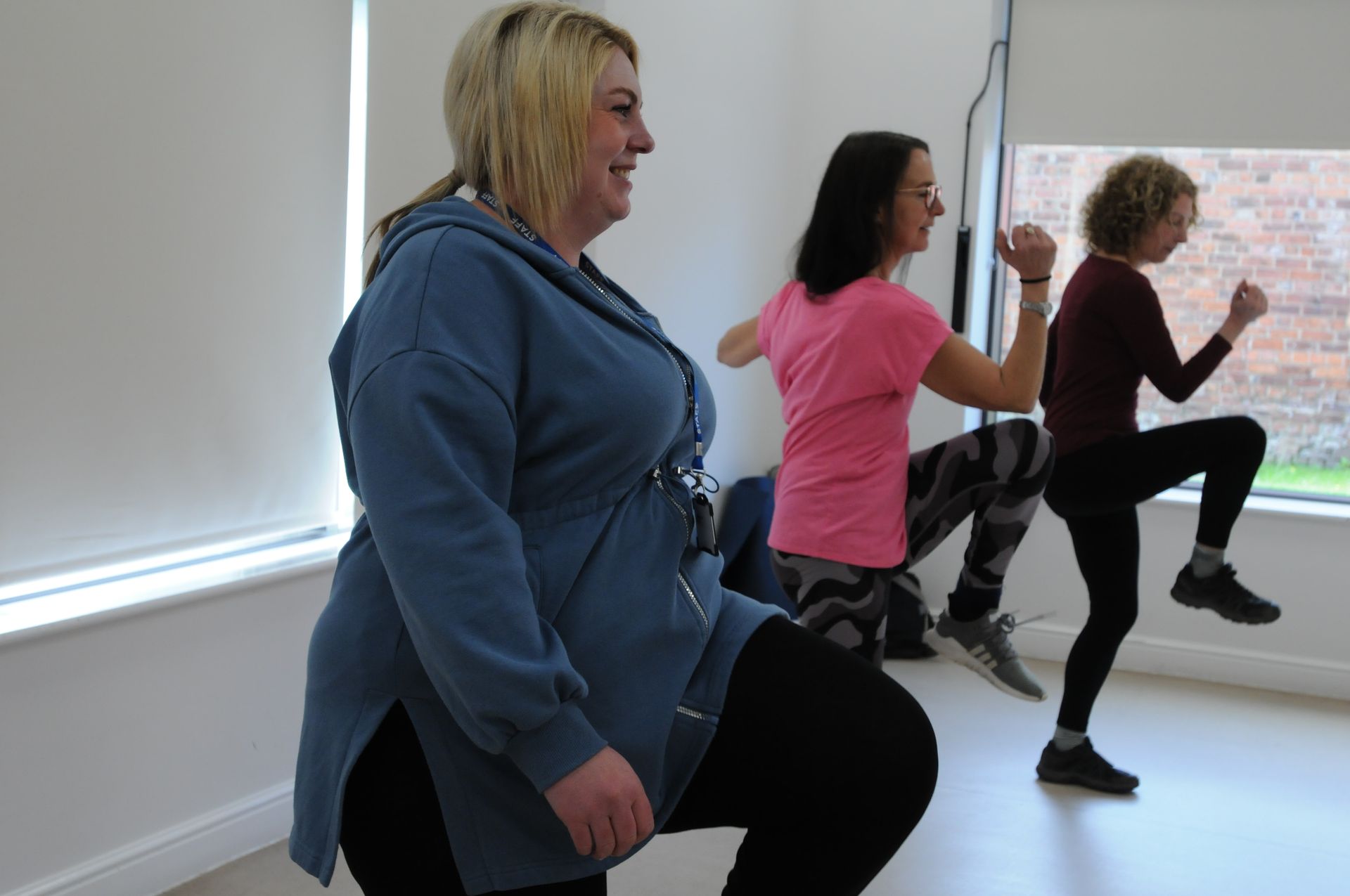 Three women are doing squats in a room in front of a window.