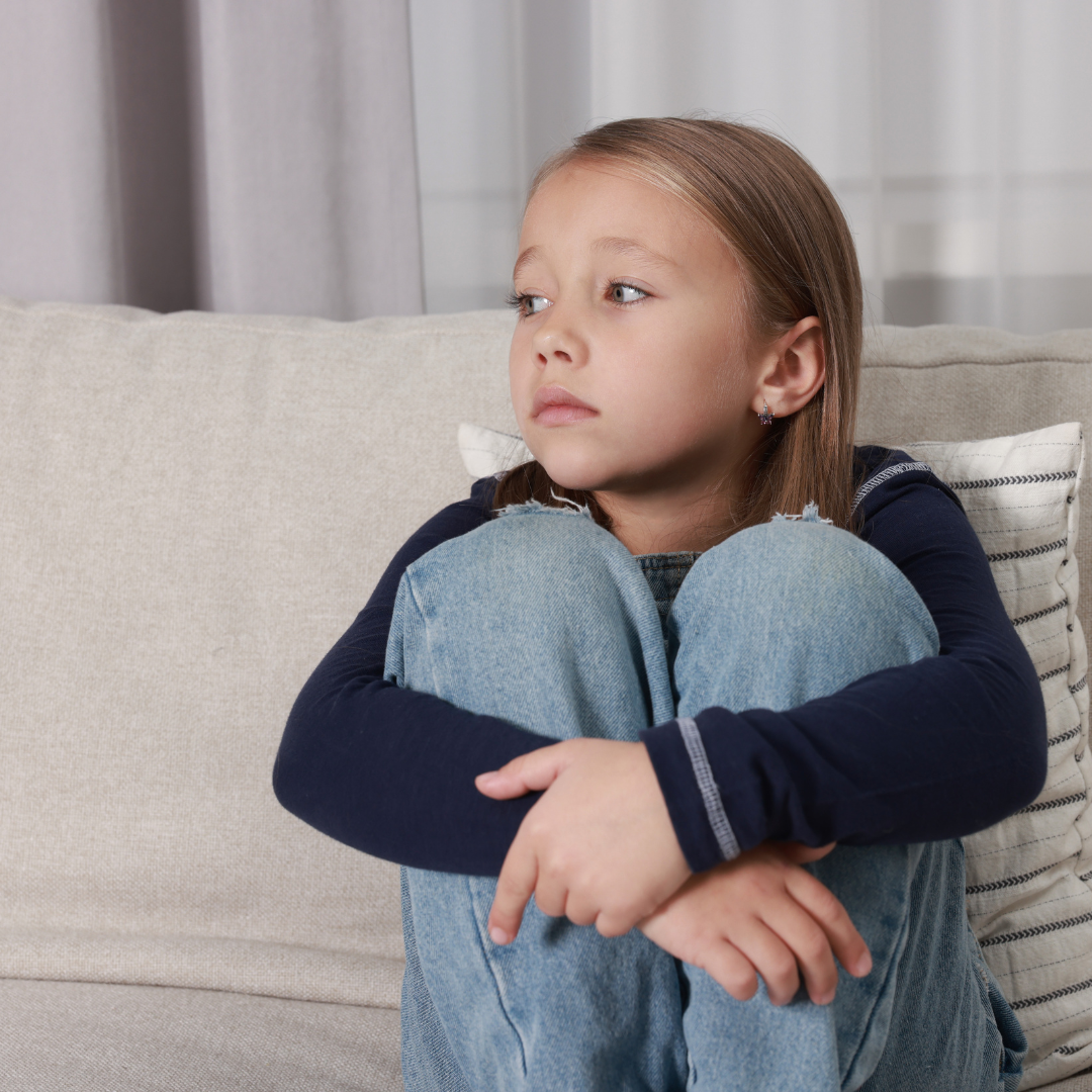 Young girl sat on her own with her arms folded around her knees
