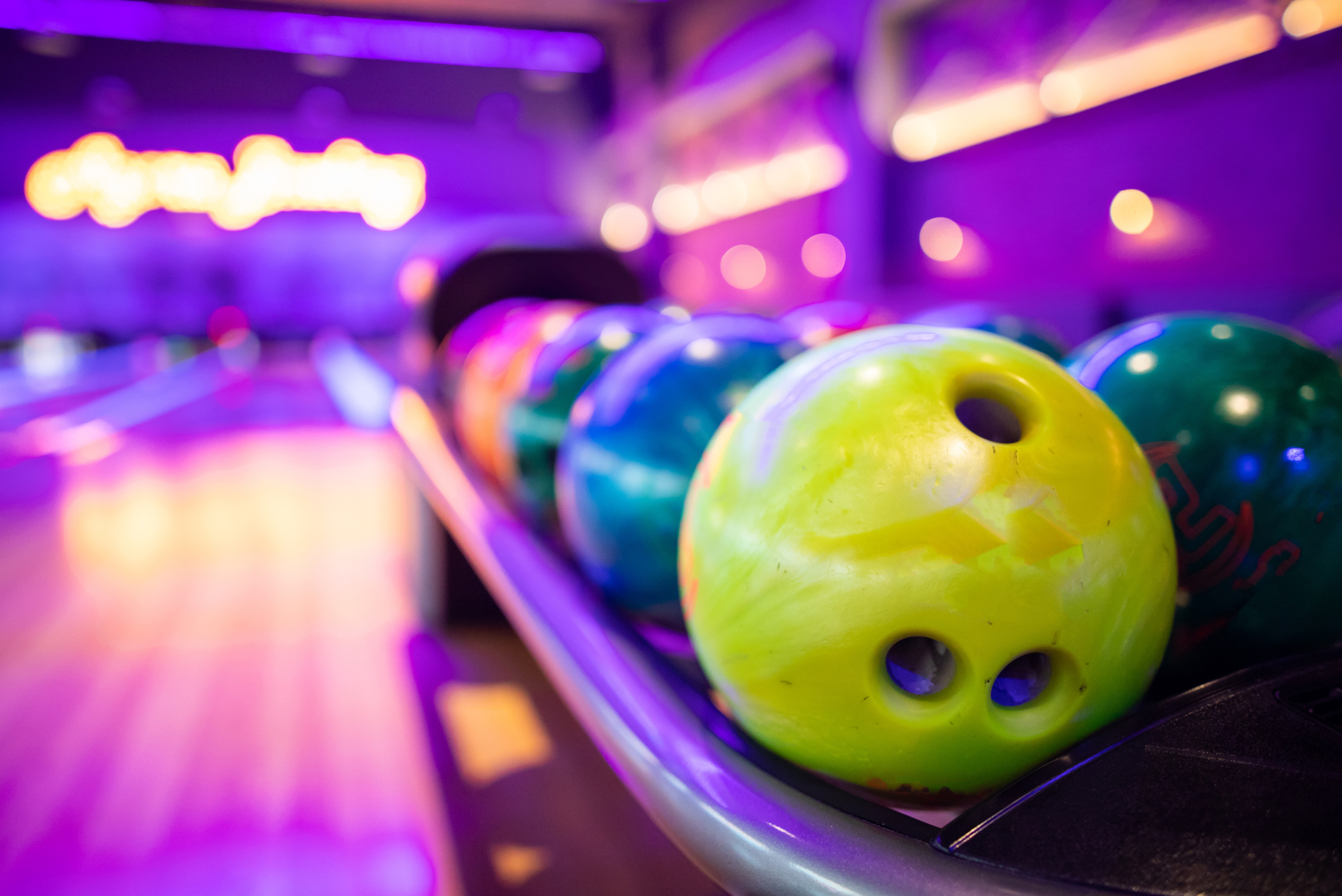 Bowling balls in a rack, colorful, bowling alley background with purple lighting.
