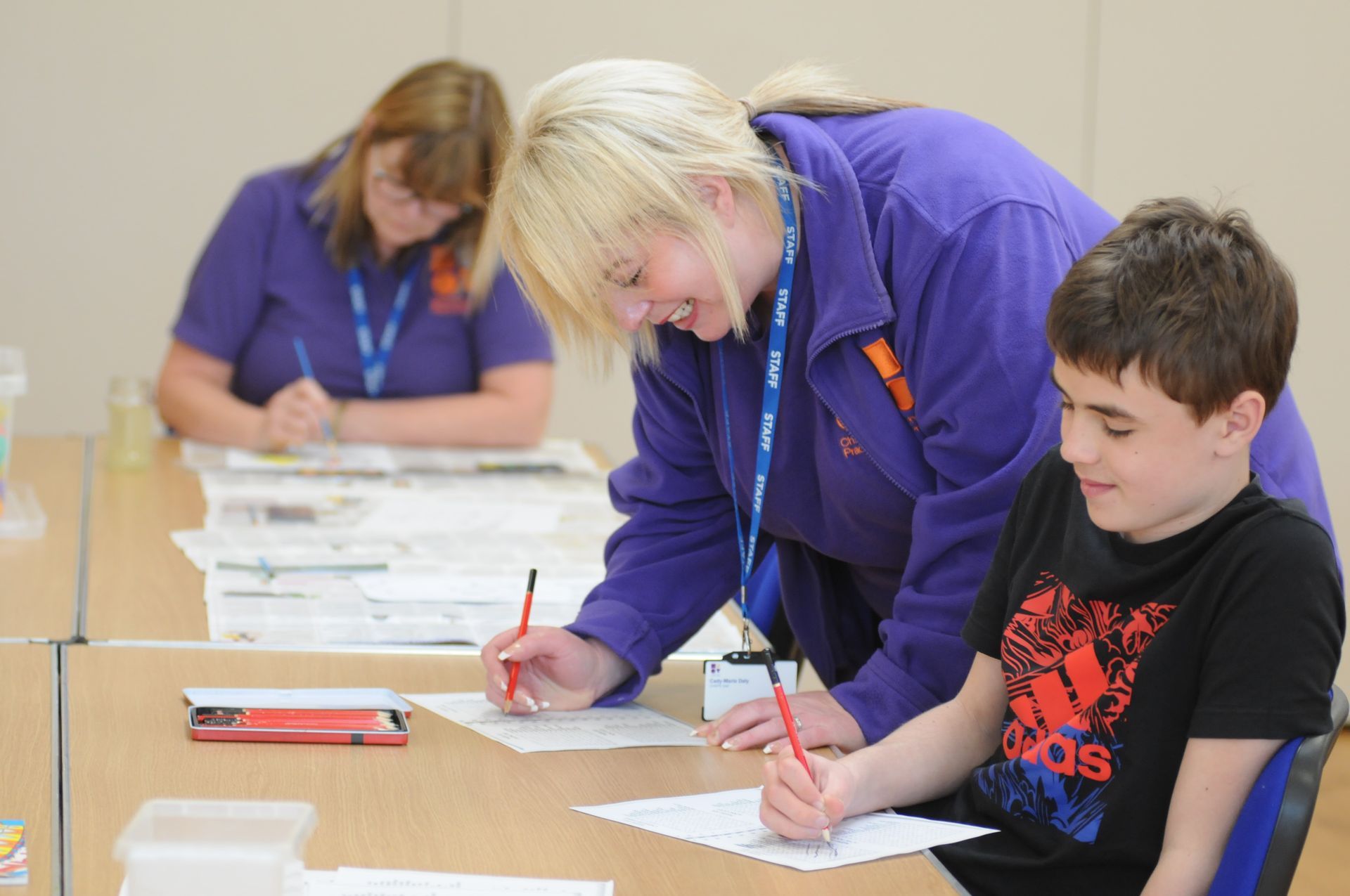 A woman is helping a boy write on a piece of paper.