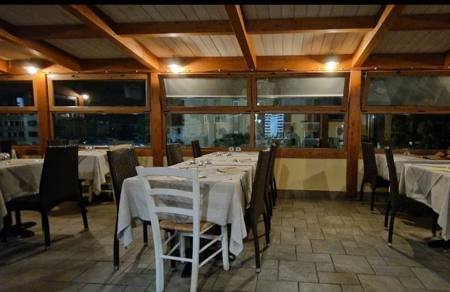 Sala da pranzo vuota di un ristorante con tovaglie bianche, travi in ​​legno e grandi finestre, di notte.