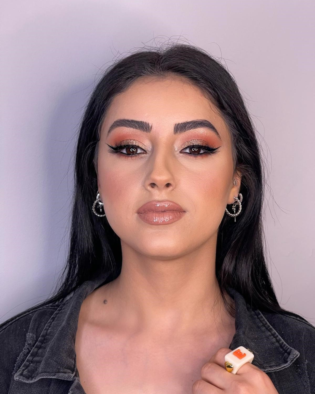 Eine Frau mit Ohrringen und einem Ring schaut in die Kamera.