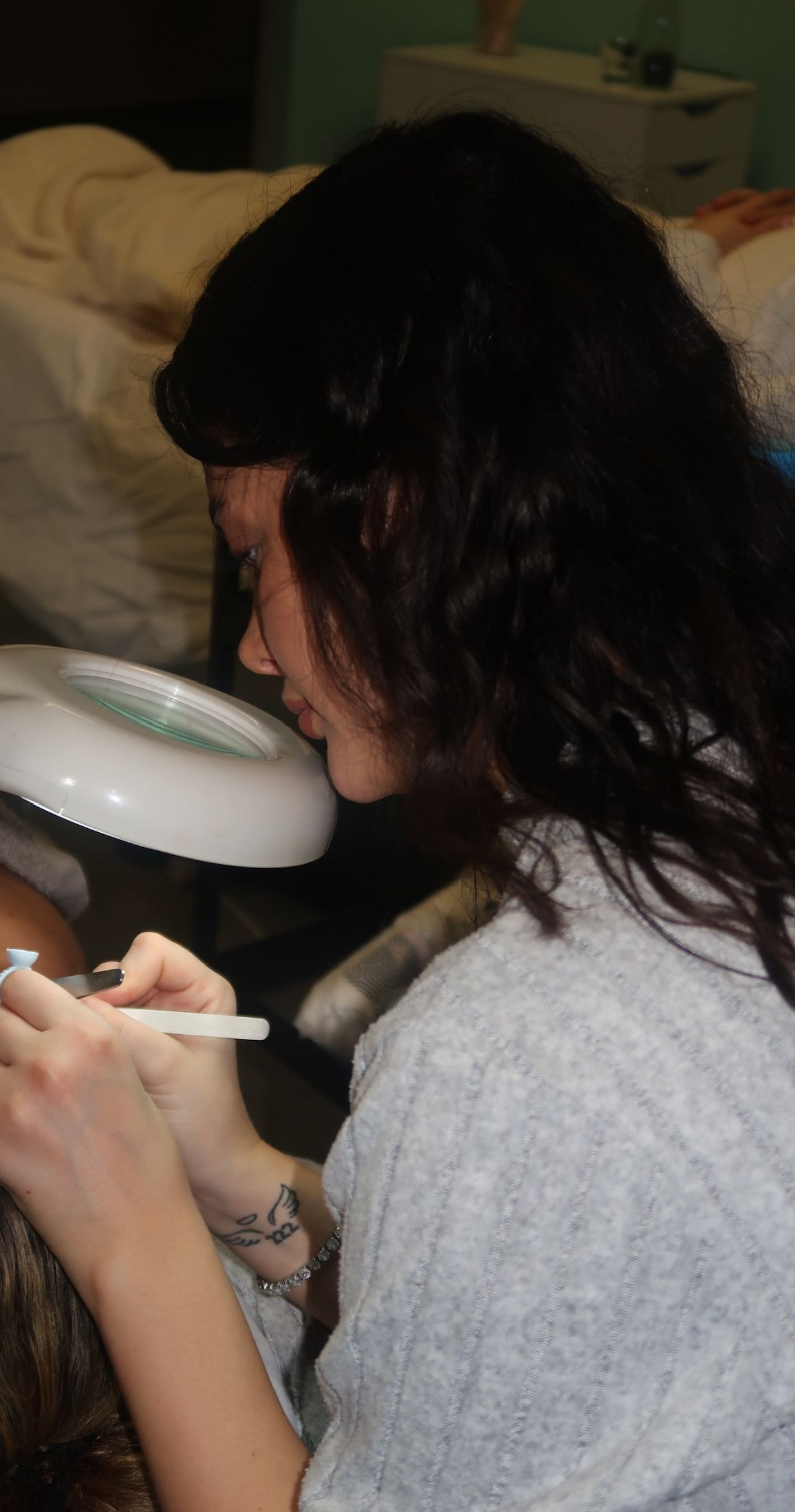 Eine Person beugt sich über eine andere Person und benutzt eine Vergrößerungslampe und ein Hilfsmittel, um deren Gesicht zu untersuchen. Spa-Atmosphäre.