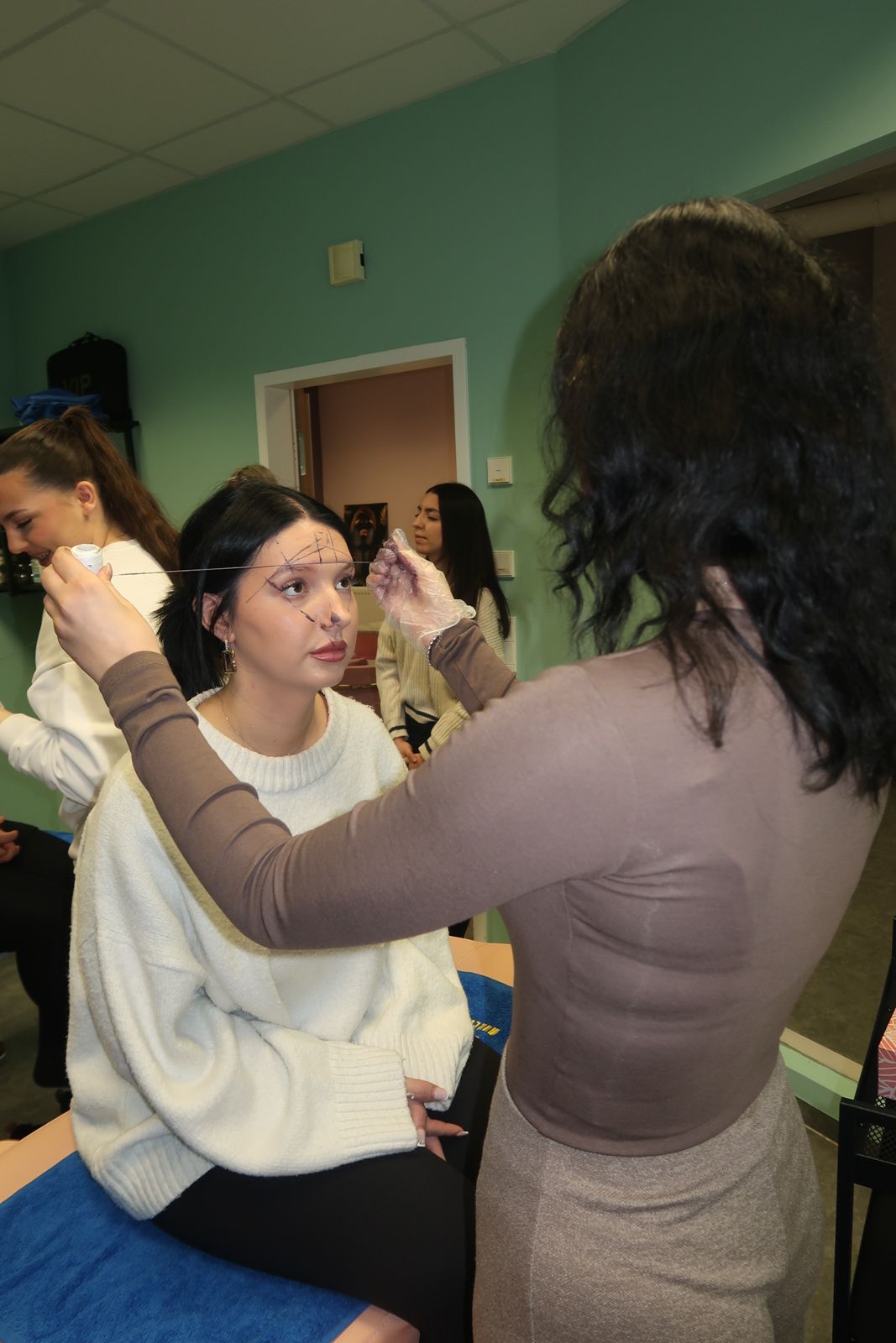 Menschen in einem Klassenzimmer, eine Person demonstriert einer anderen das Schminken.