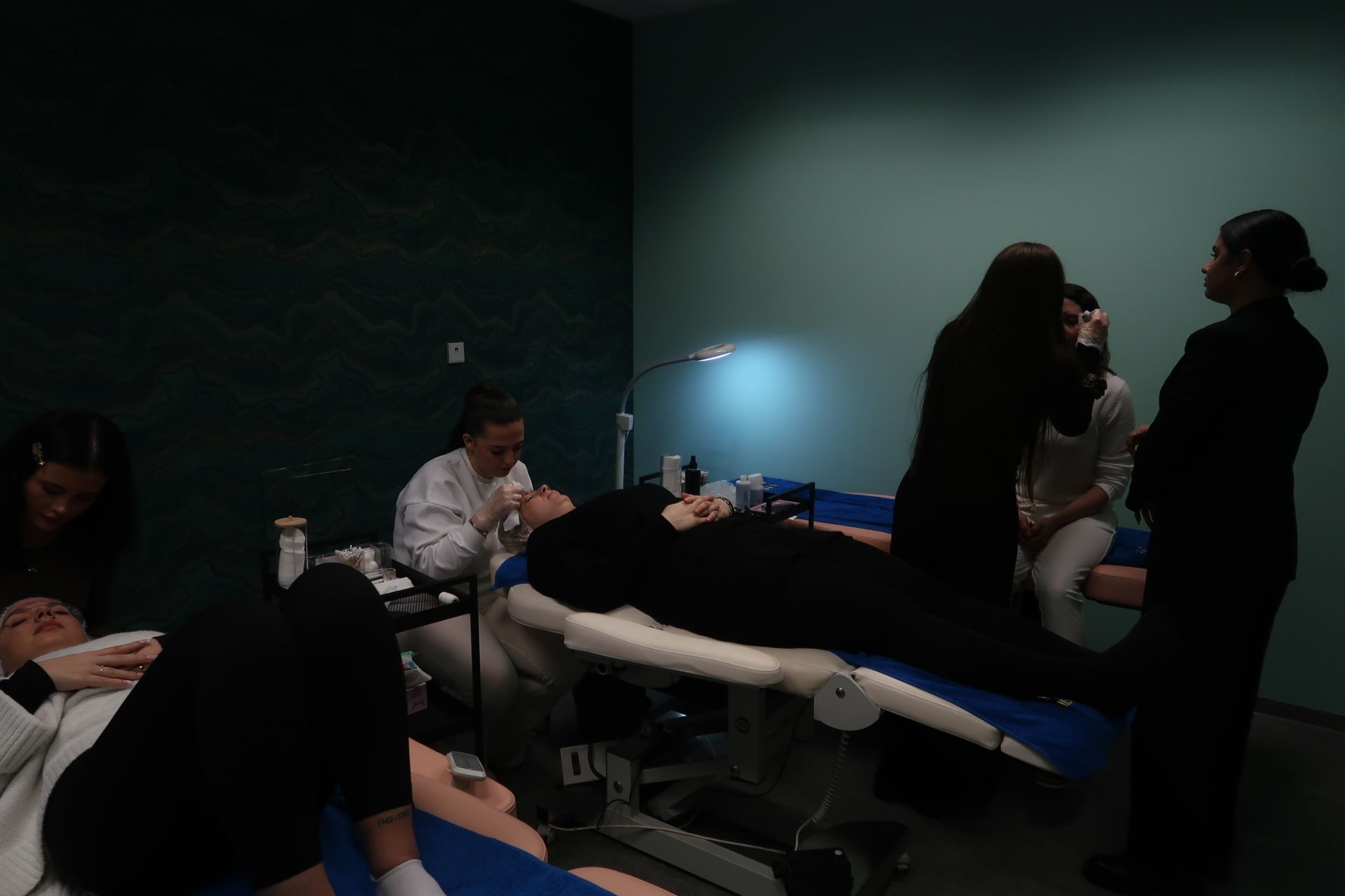 Teilnehmer eines Kosmetikkurses; eine Schülerin erhält eine Gesichtsbehandlung. Andere Schüler beobachten die Behandlung.