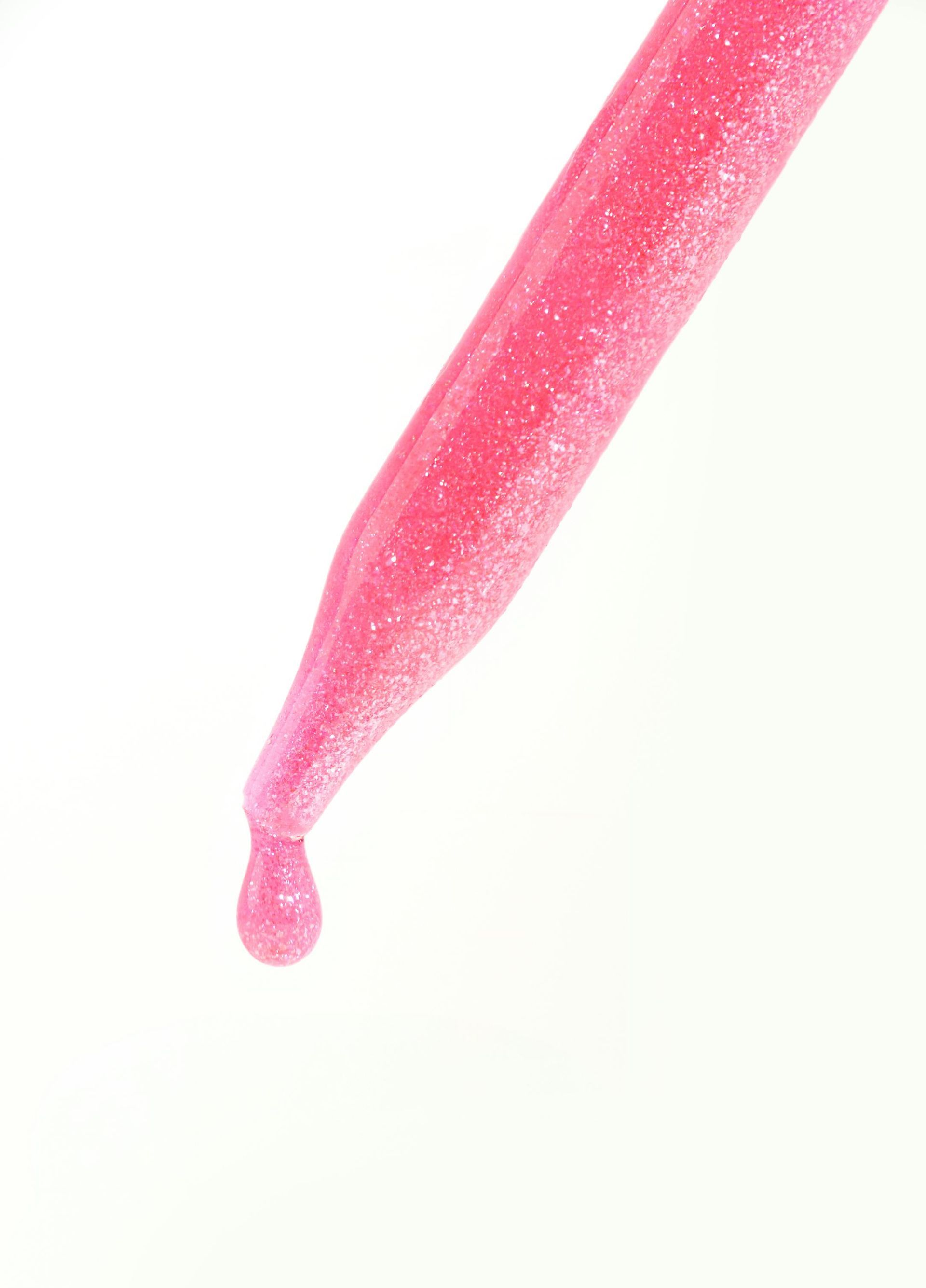 Eine Nahaufnahme einer rosa Pipette, aus der ein Tropfen Flüssigkeit herauskommt.