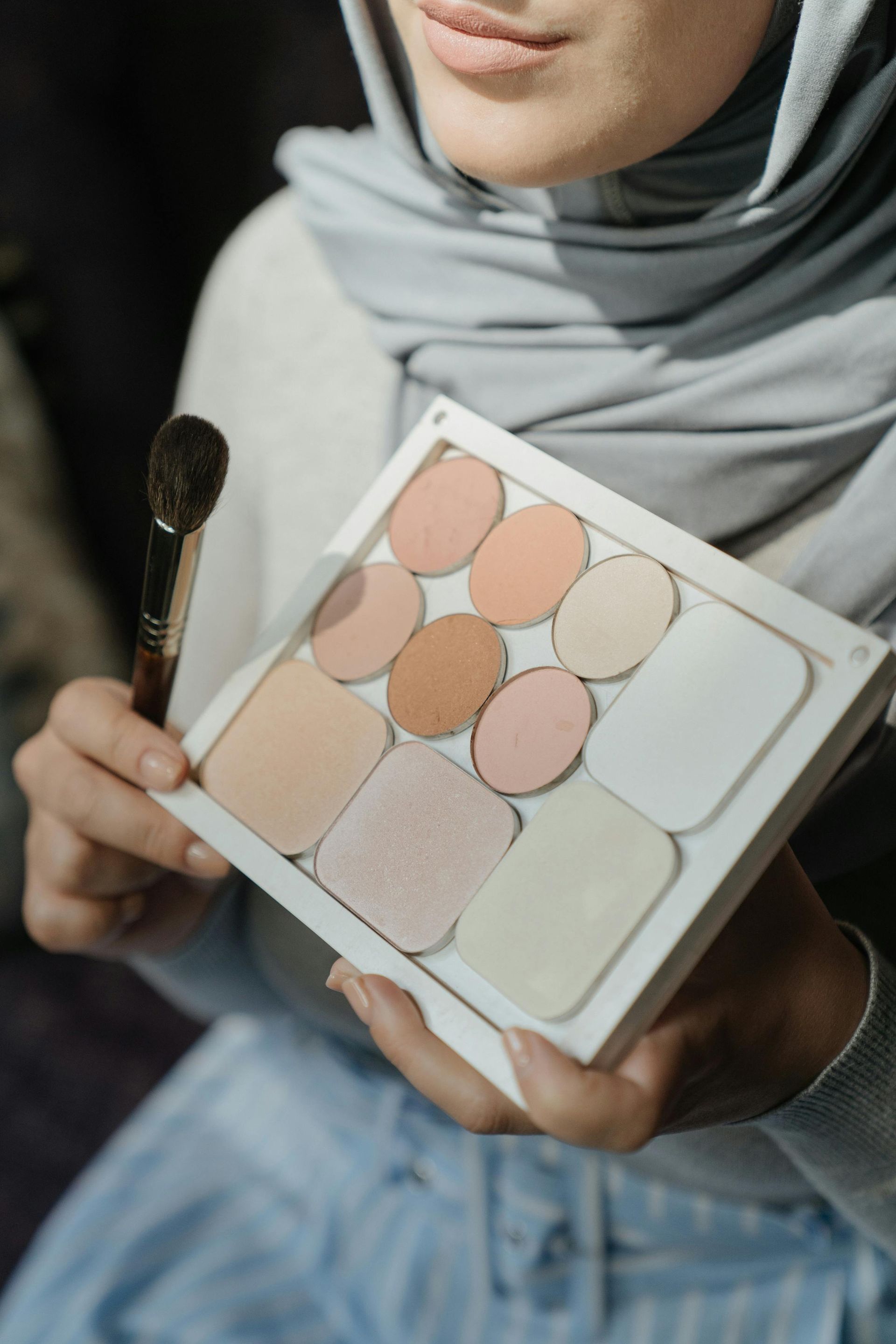 Eine Frau mit Hijab hält eine Make-up-Palette und einen Pinsel in der Hand.