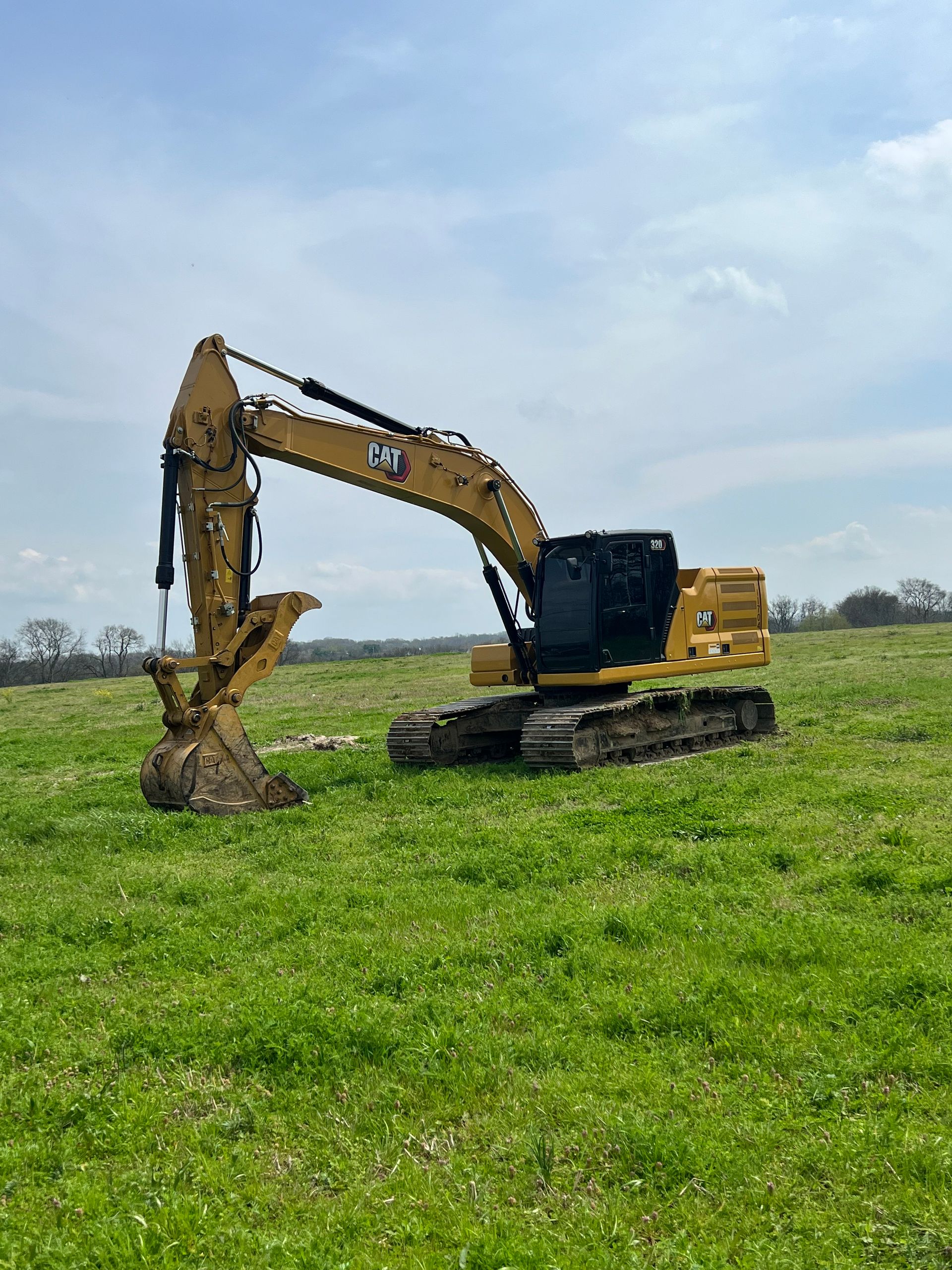 A large excavator is sitting in the middle of a grassy field.