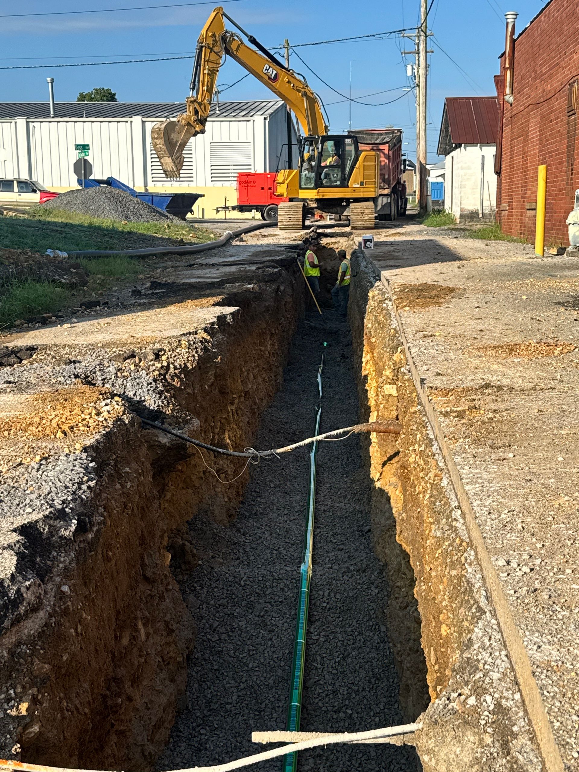 A yellow excavator is digging a hole in the ground next to a brick building.