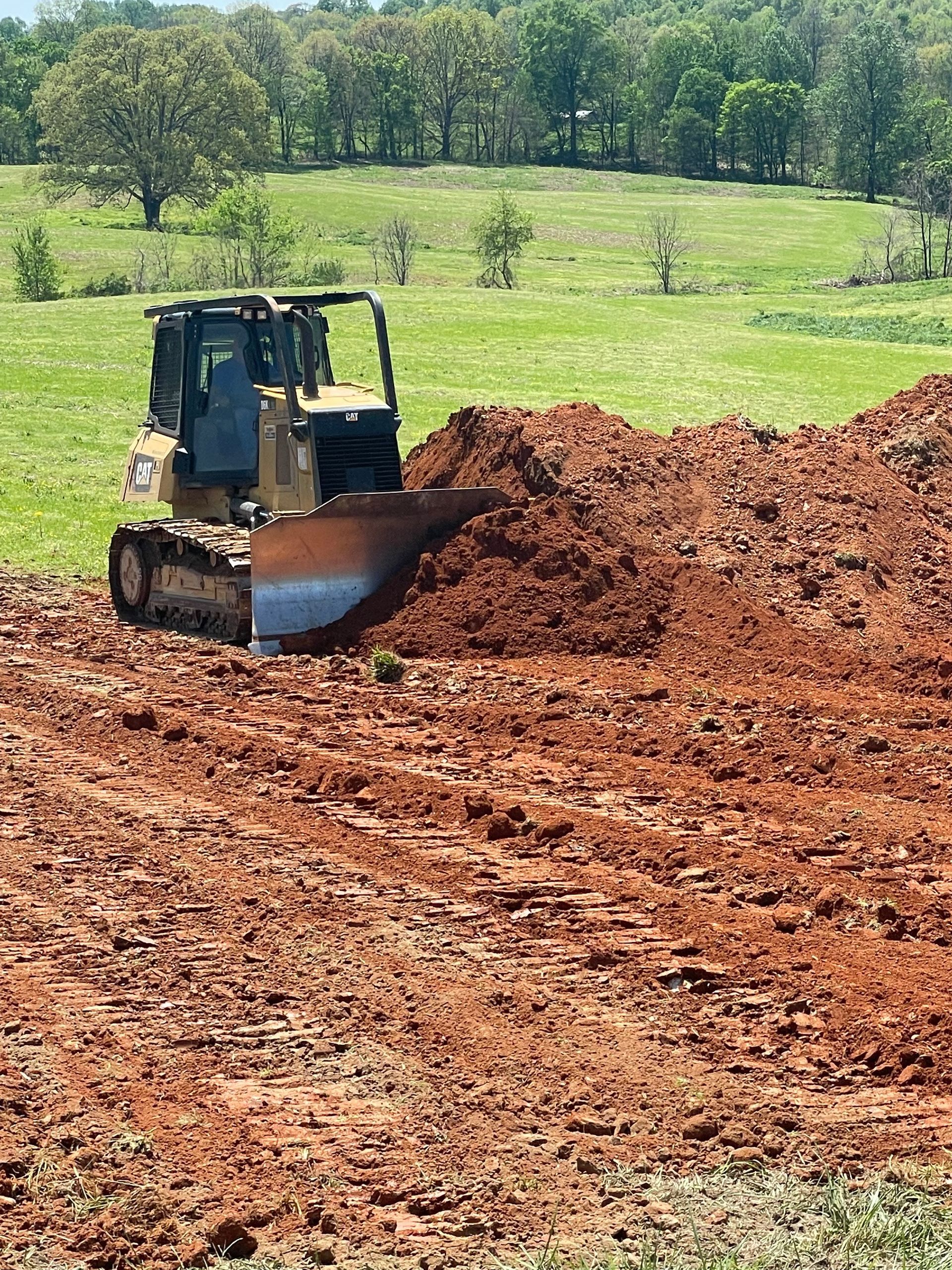 A red dump truck is driving down a dirt road next to an excavator.