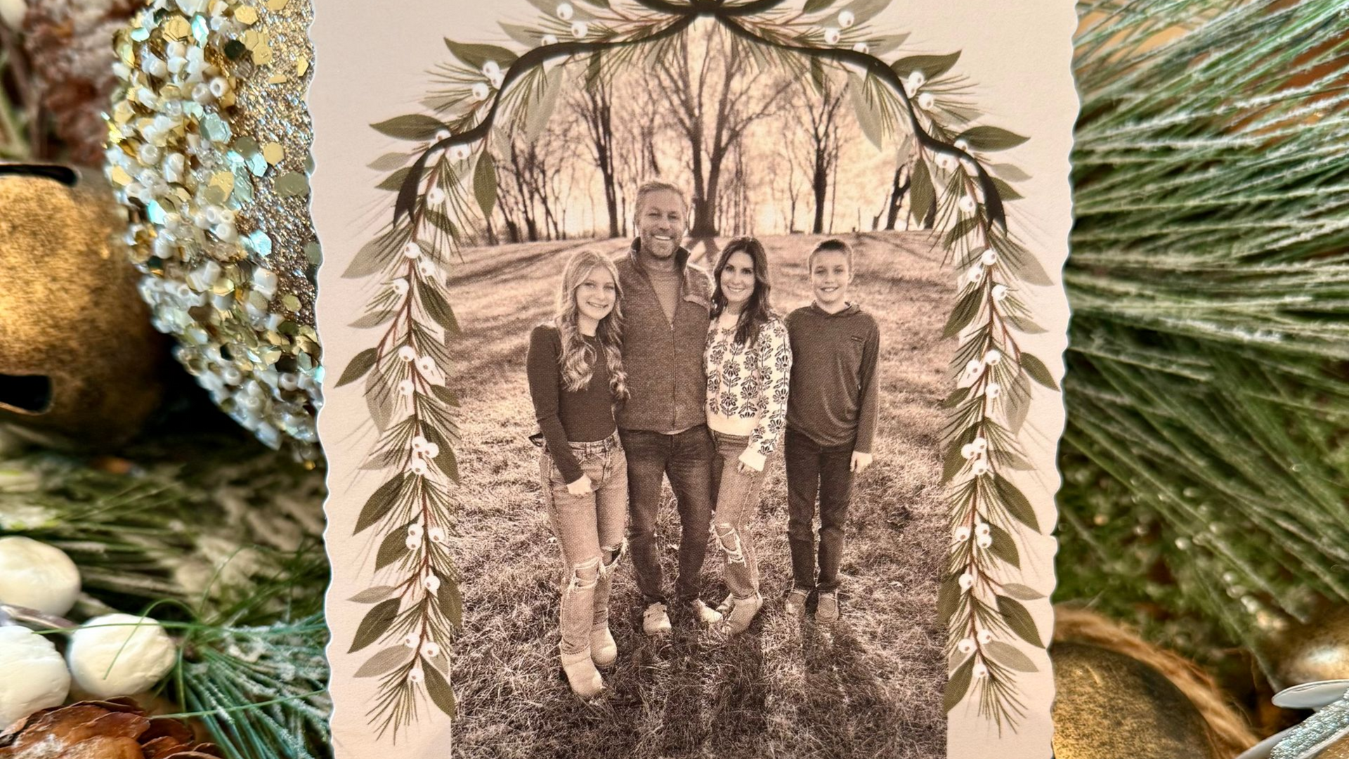 Family portrait in sepia tones, framed by leaves. People stand in a park-like setting.