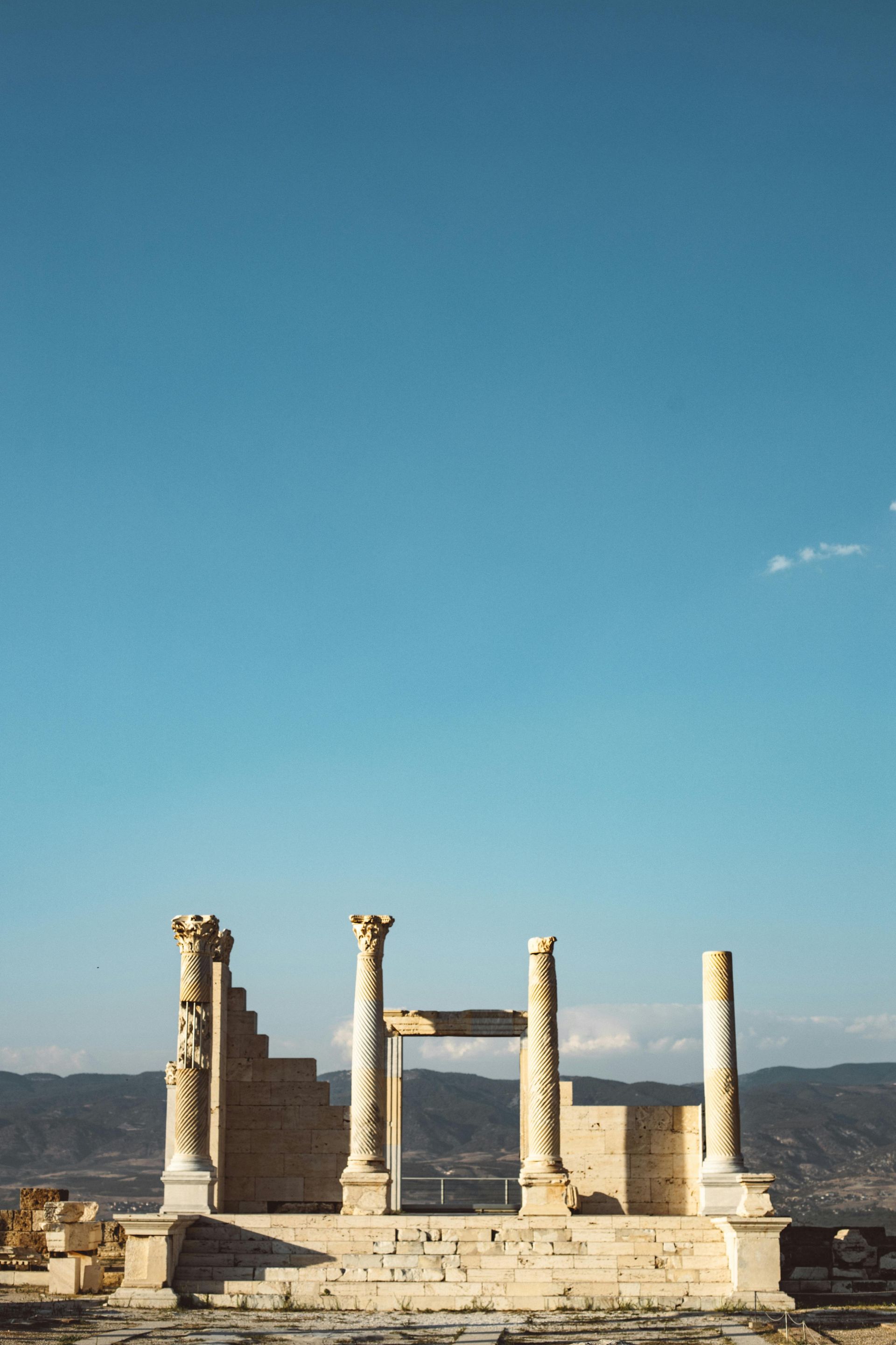 A row of columns in front of a blue sky with mountains in the background.
