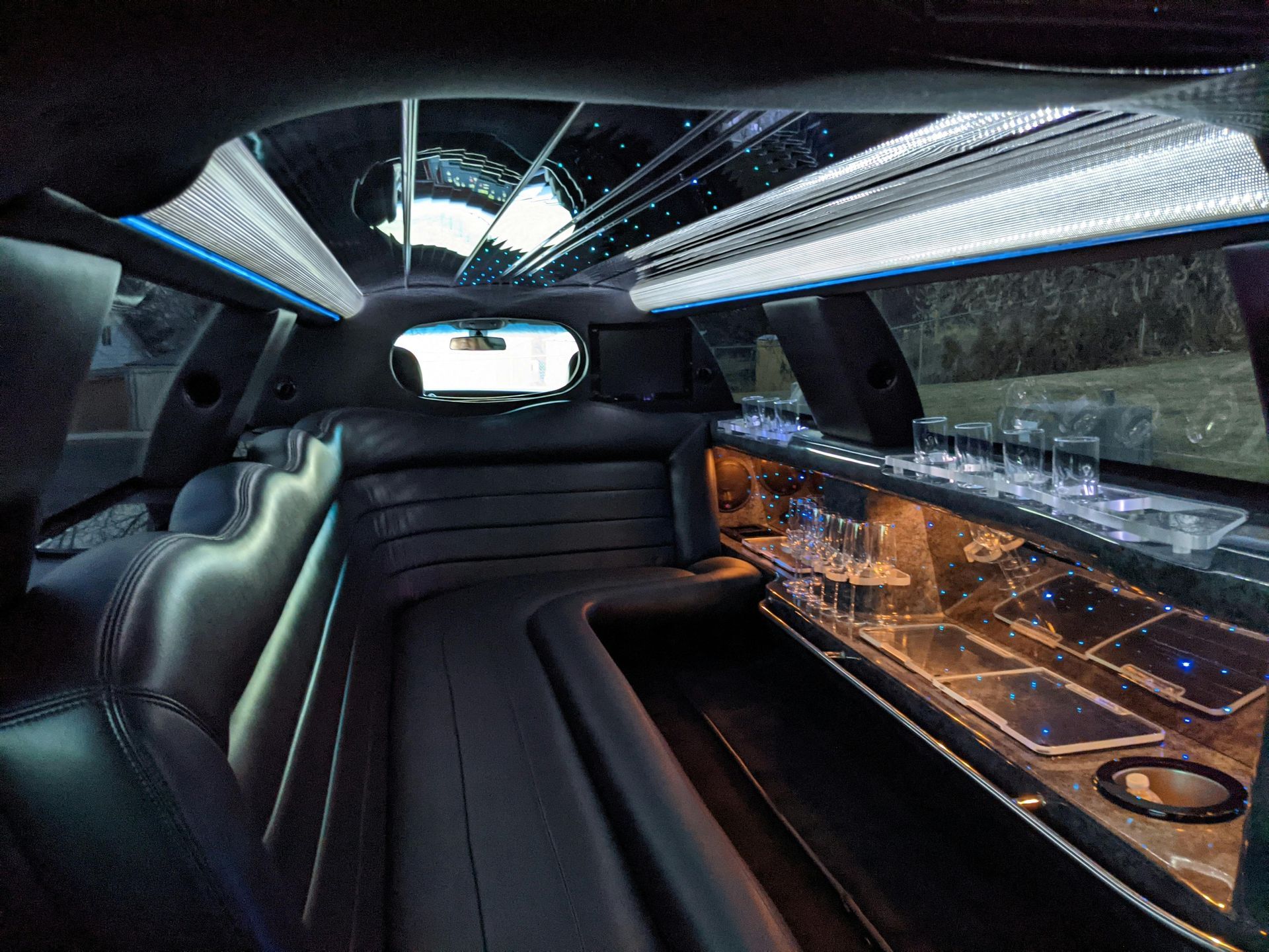 Interior of a black limousine with leather seating, a bar area, and illuminated ceiling.