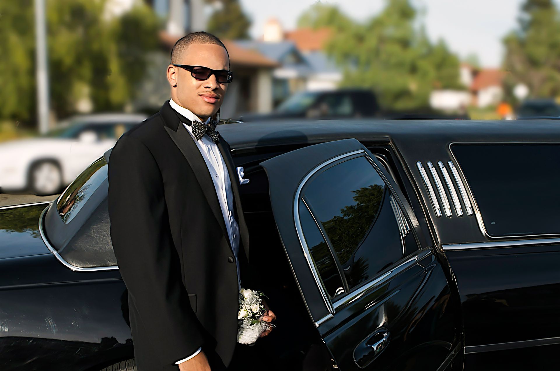 A man in a tuxedo is standing next to a black limousine