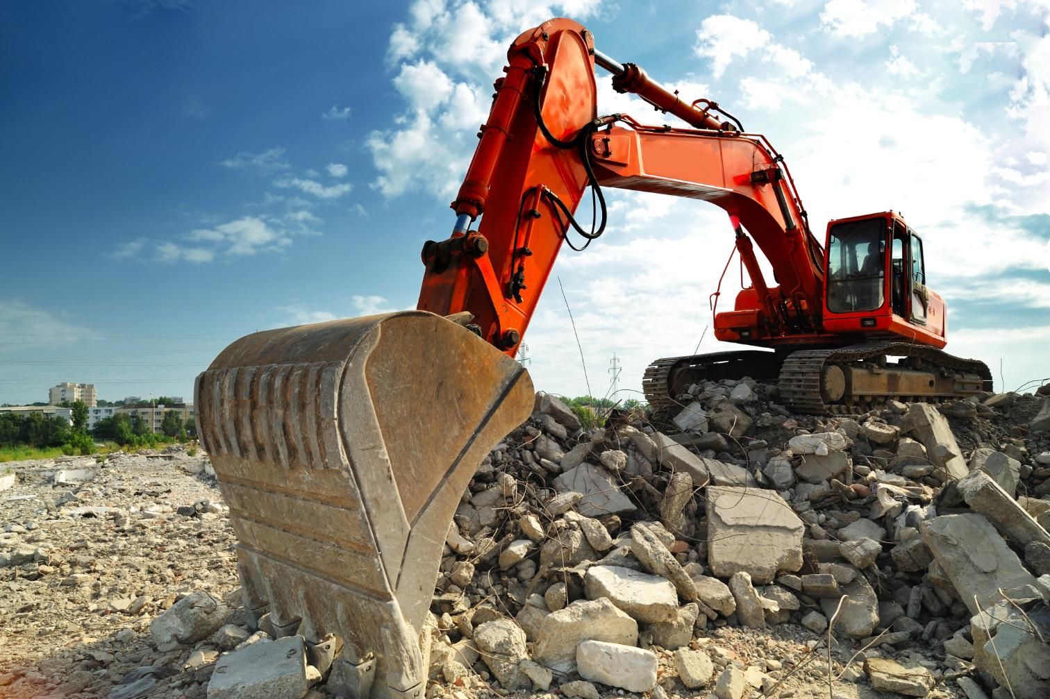 Orange excavator digging through a pile of rubble under a blue sky
