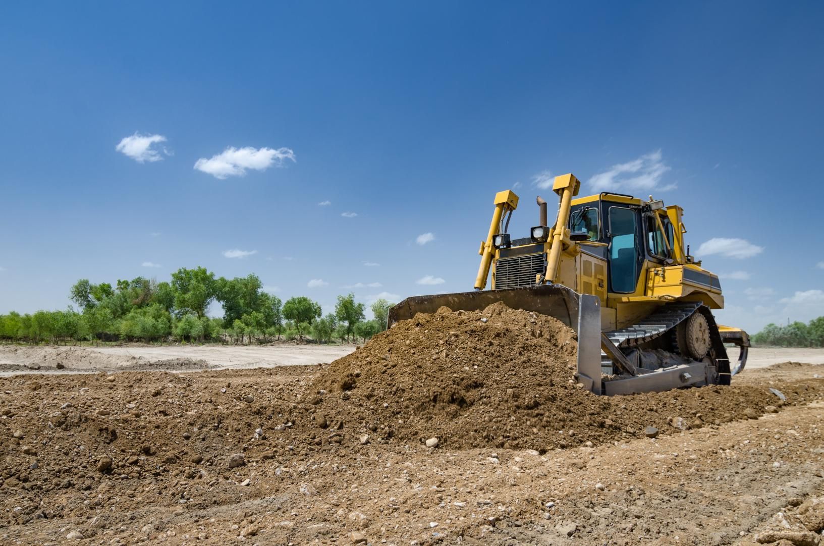 Yellow bulldozer pushing dirt on a construction site under a blue sky