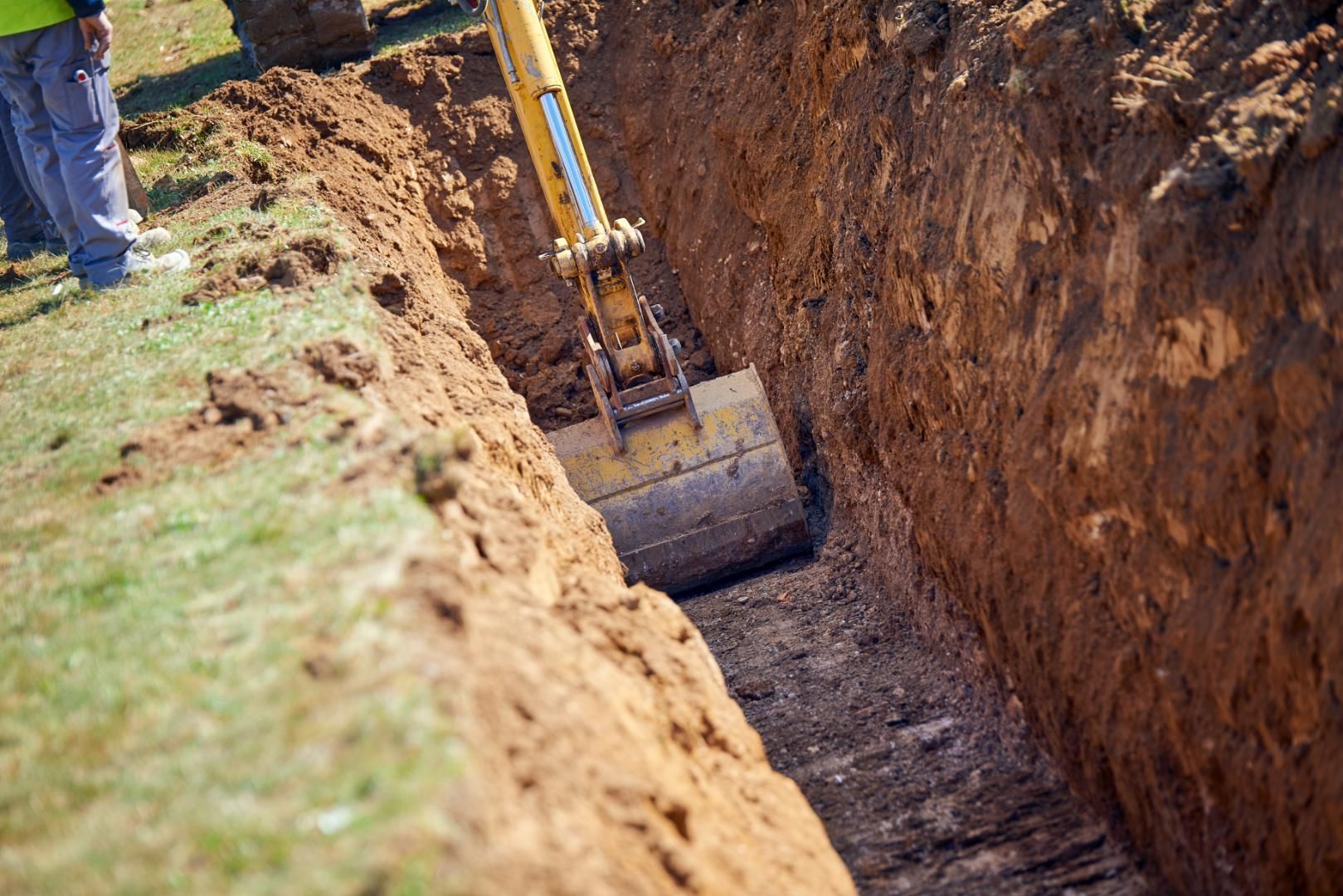 Excavator digging a deep trench beside a grassy edge