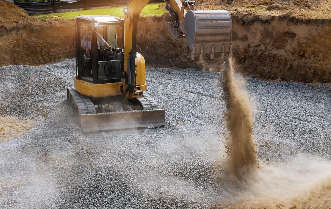 Excavator spraying water at a gravel excavation site, creating a dusty splash.