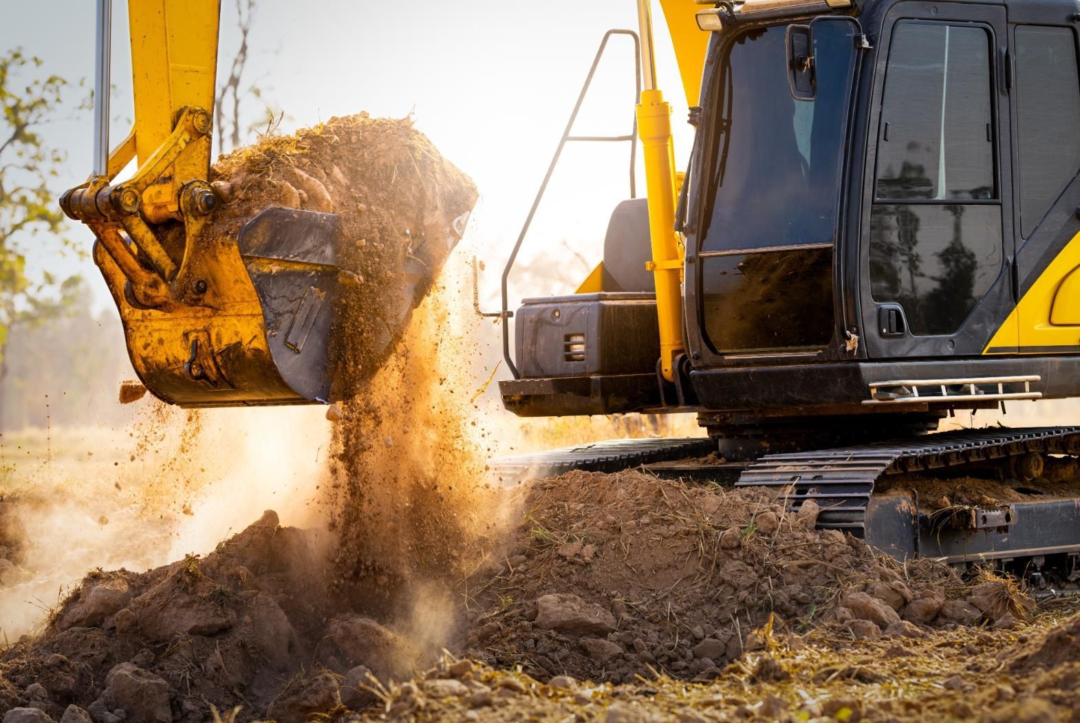 Excavator dumping dirt at a construction site at sunset