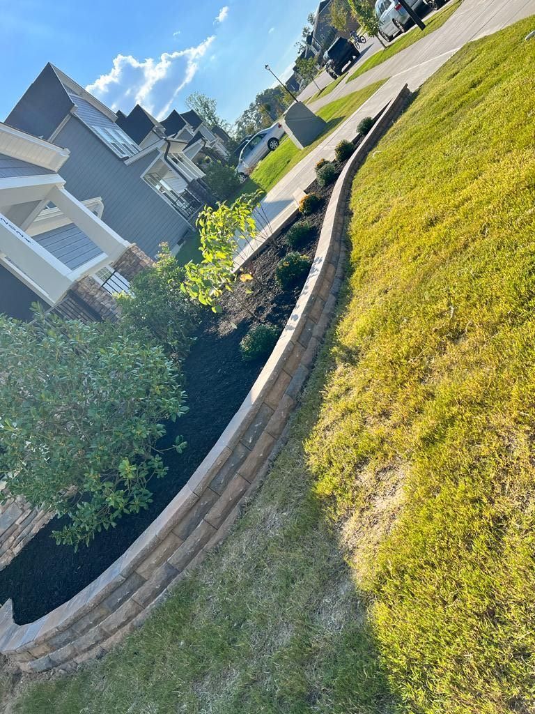 A brick wall surrounds a lush green lawn in front of a house.