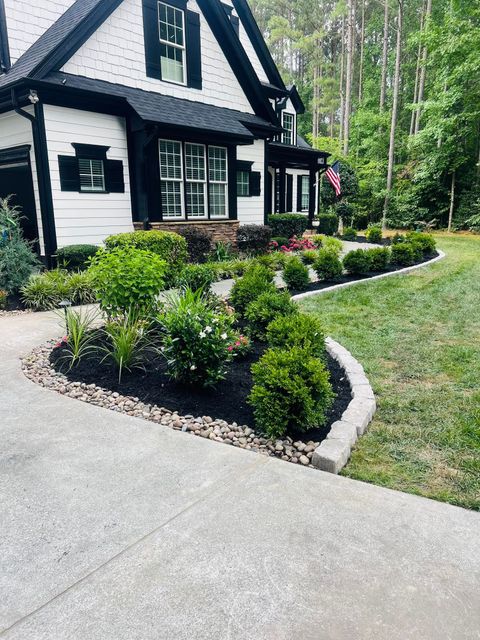 A black and white house with a lush green lawn and bushes in front of it.