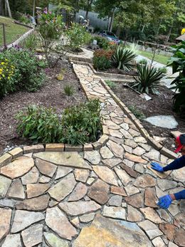 A person is working on a stone walkway in a garden.