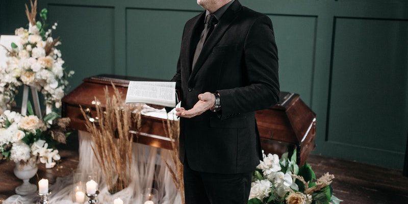 a man in a suit is standing in front of a coffin at a funeral .