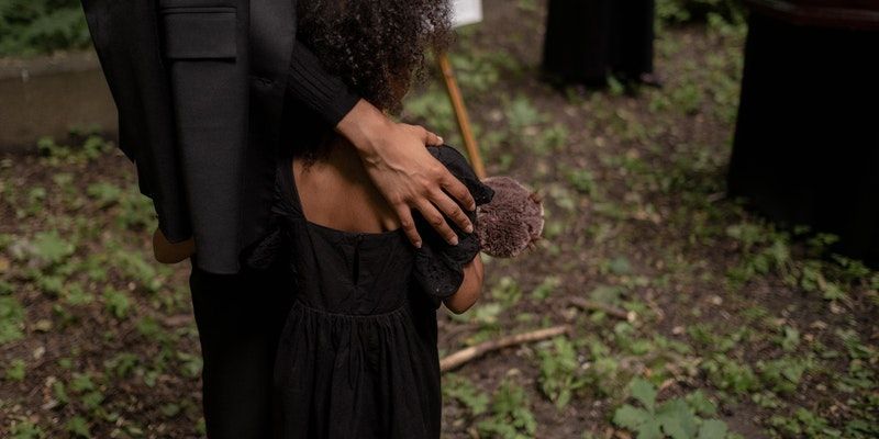 a woman in a black dress is hugging a child in front of a coffin .