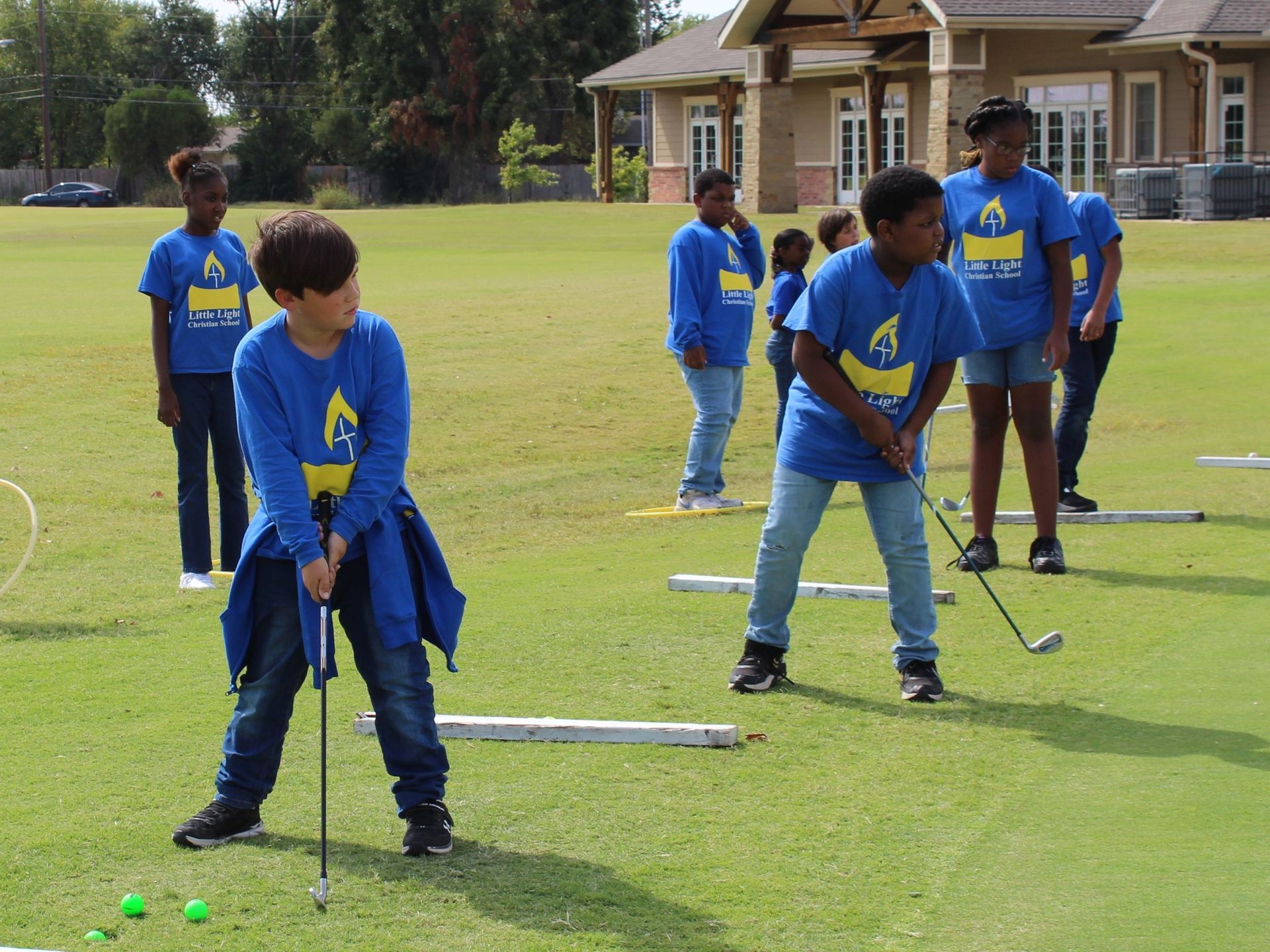 People in blue shirts practicing golf swings on a grassy field near houses