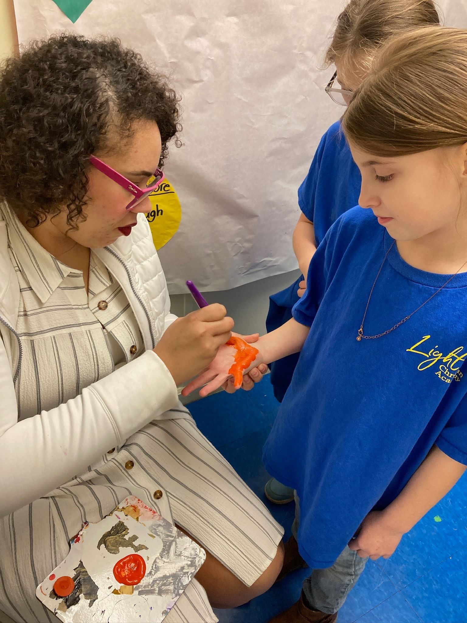 Woman paints a child's hand orange while the child watches