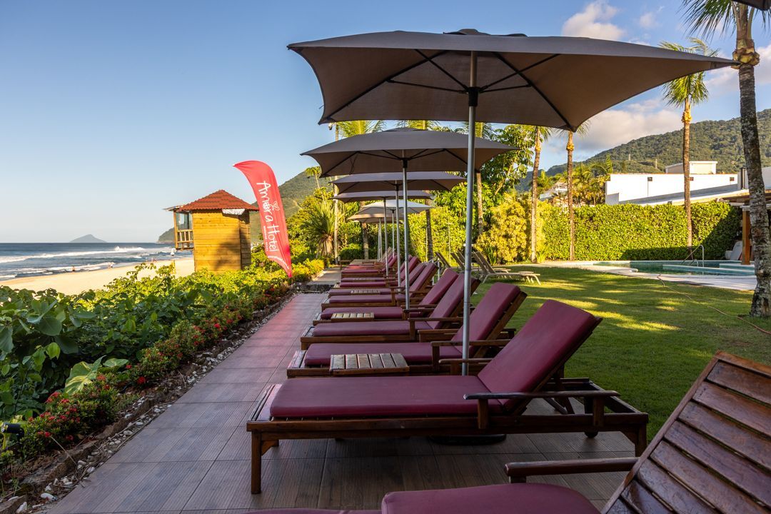 Uma fileira de espreguiçadeiras e guarda-sóis estão alinhados em frente a uma piscina.