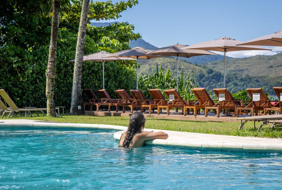 Uma mulher está sentada em uma piscina cercada por cadeiras e guarda-sóis.