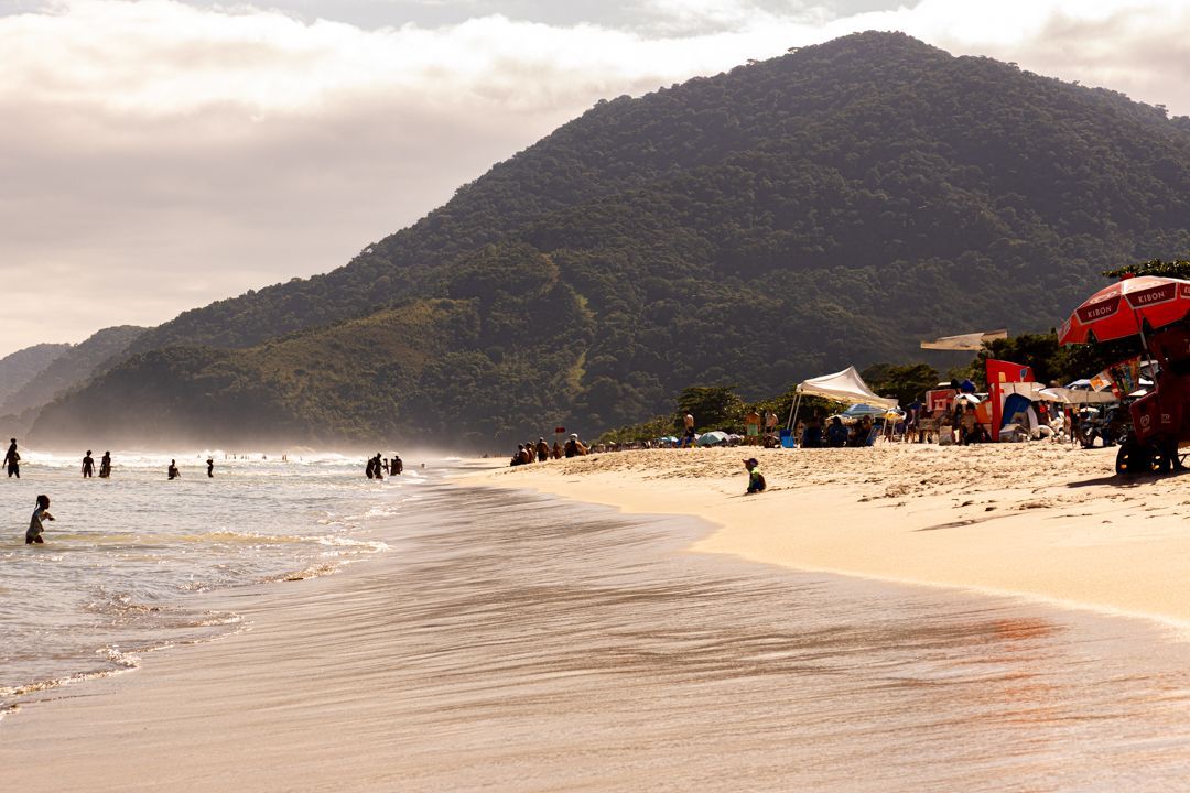 Um grupo de pessoas está nadando no oceano em uma praia com montanhas ao fundo.