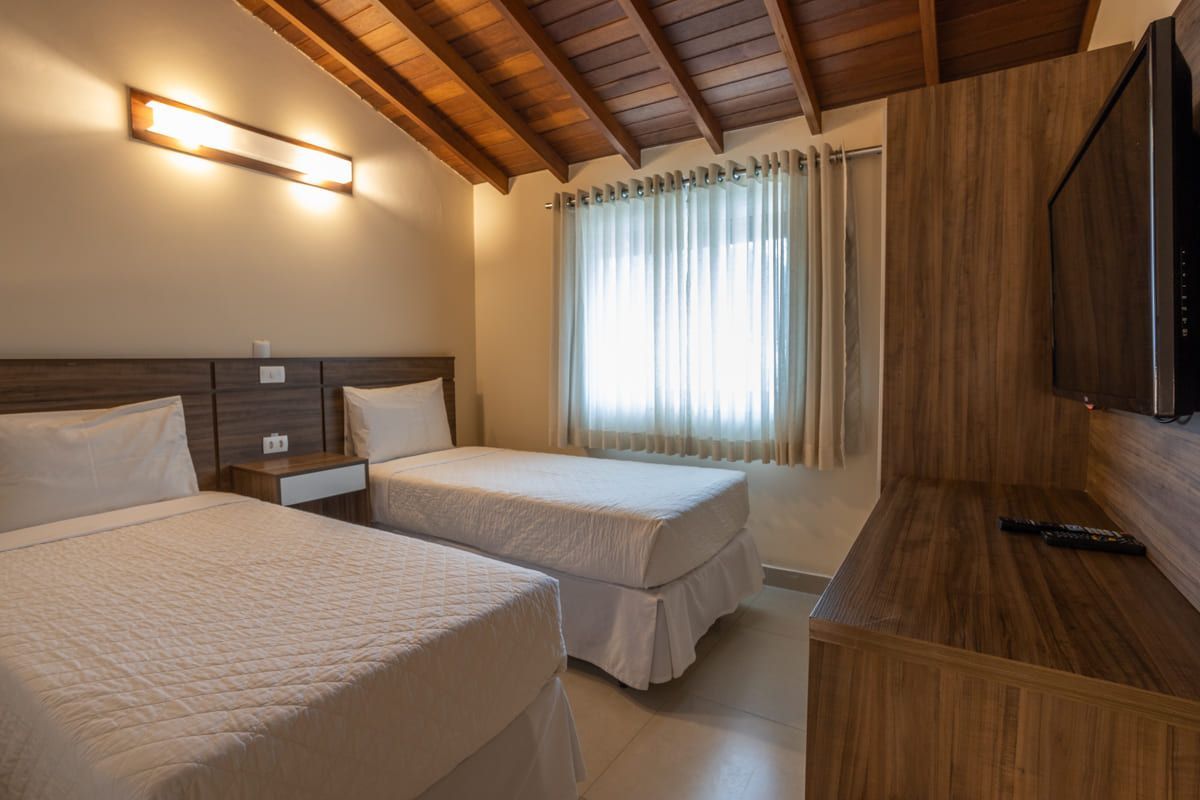 Um quarto de hotel com duas camas, uma televisão e um teto de madeira.