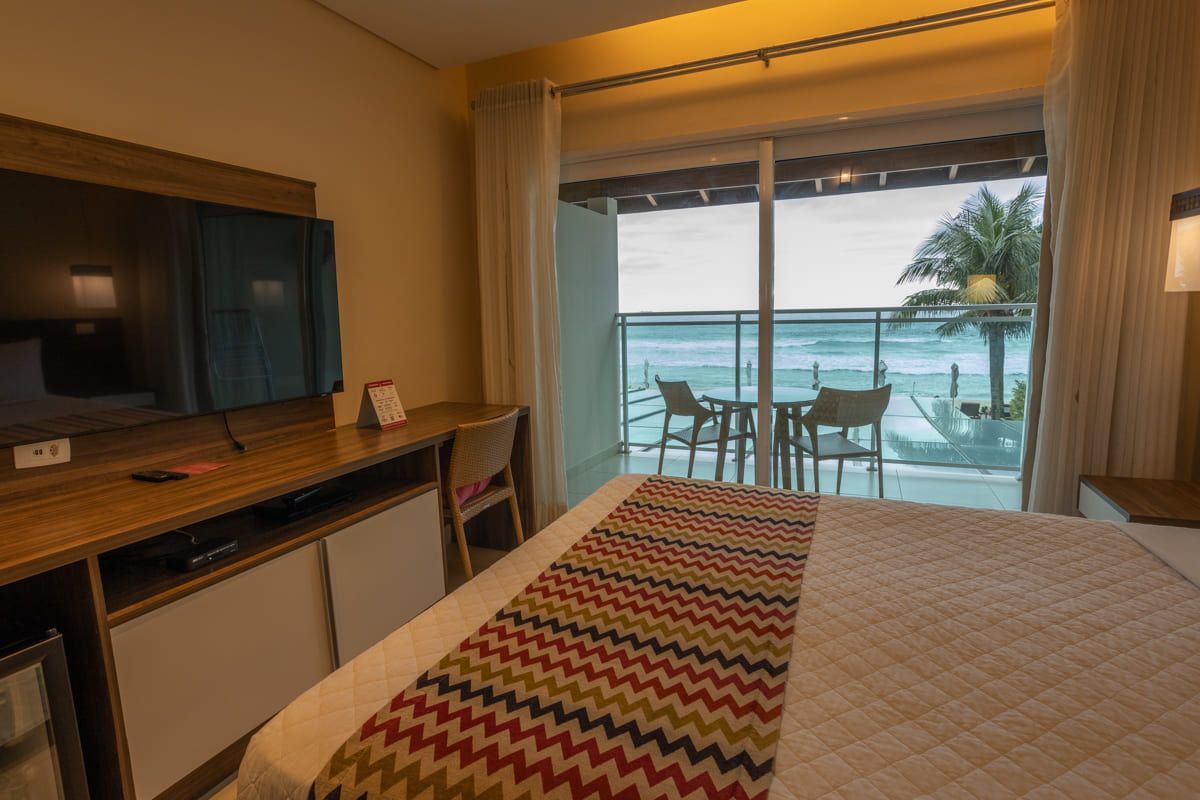 Um quarto de hotel com cama, televisão, escrivaninha e varanda com vista para o oceano.