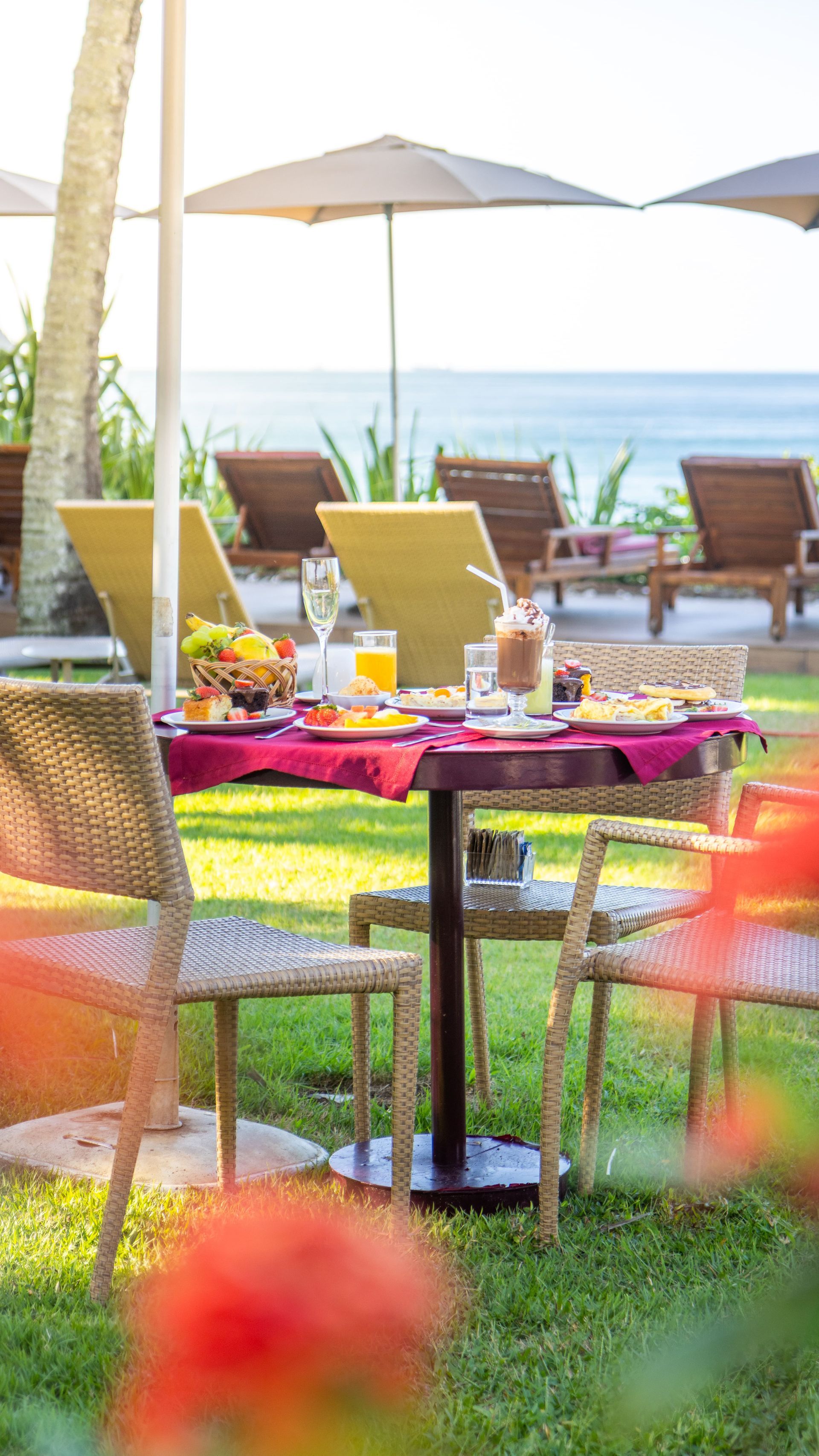 Há uma mesa e cadeiras na grama com guarda-sóis ao fundo.