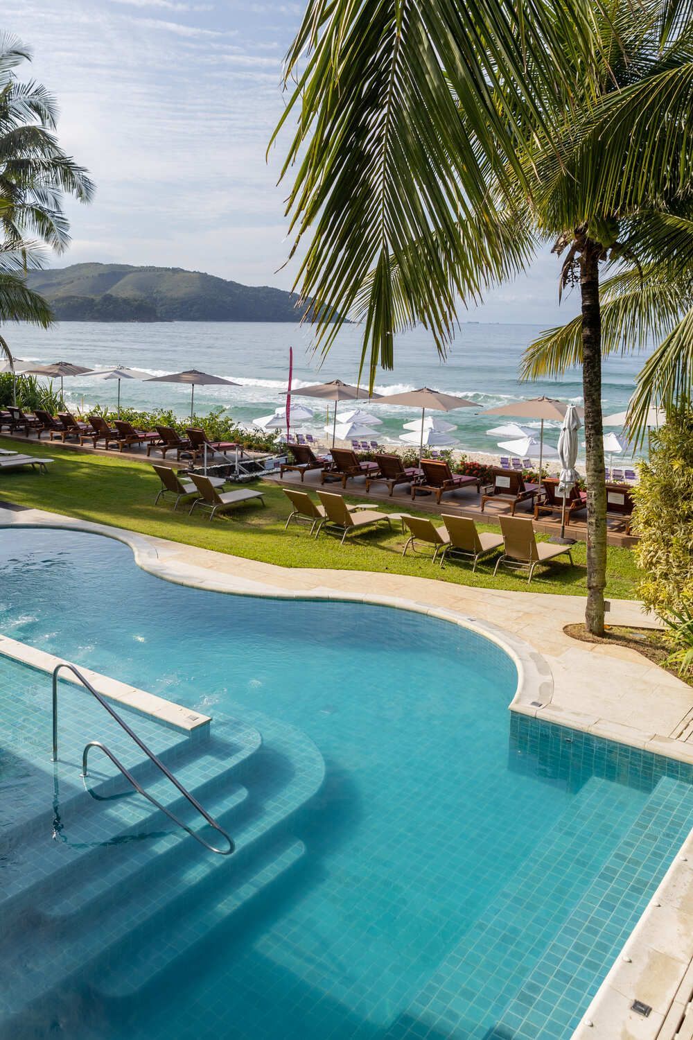 Uma grande piscina cercada por cadeiras e guarda-sóis ao lado de uma praia.